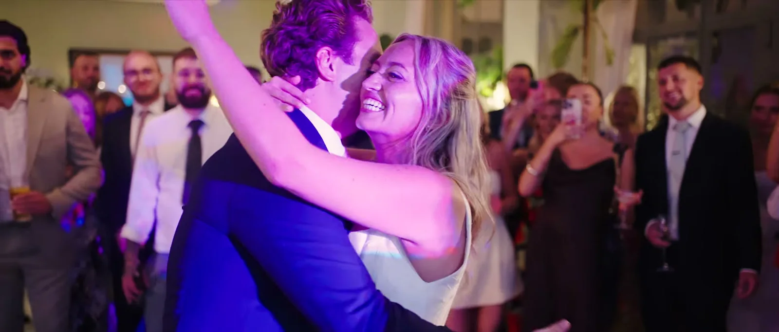 A bride laughs with her arms in the air as her groom holds her close on the dance floor