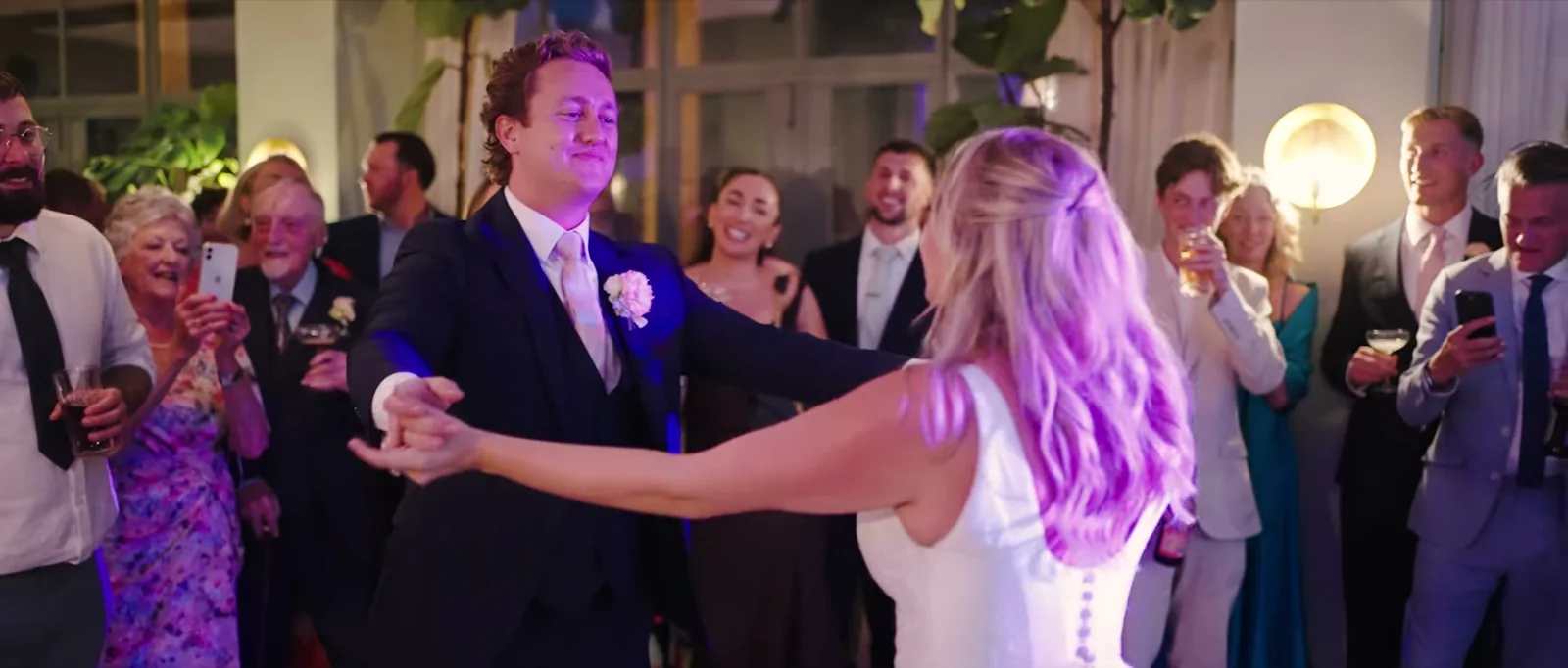A groom turns his bride in their first dance while guests look on with their phones raised