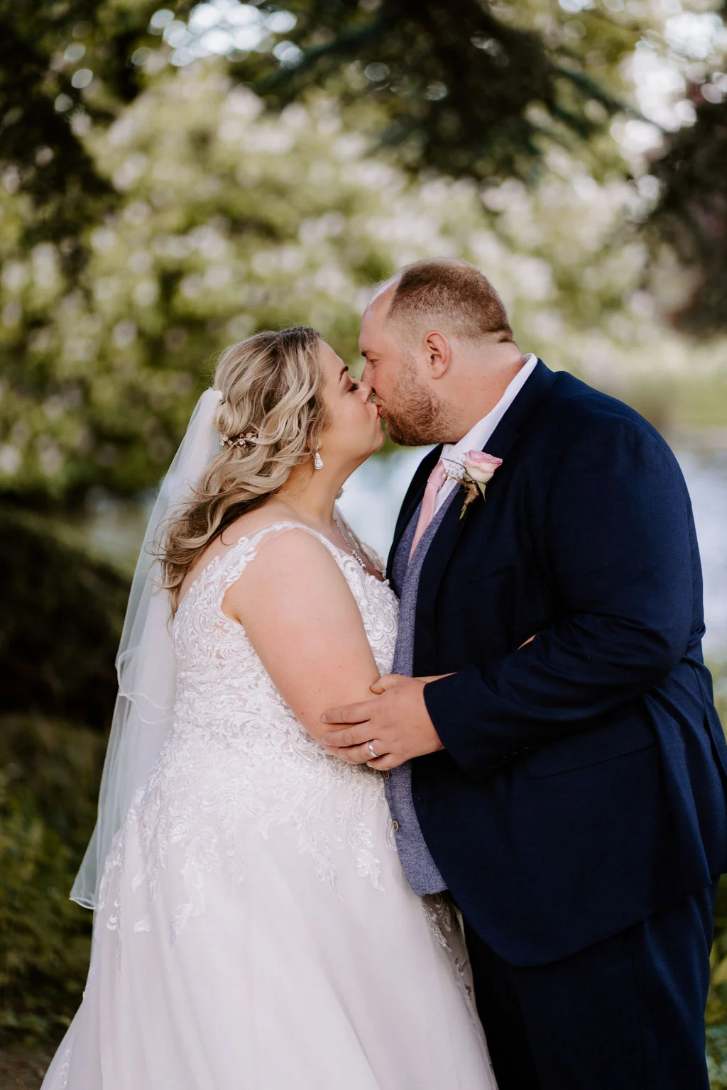 Emma and Jason kissing beneath the trees in the grounds of Dumbleton Hall