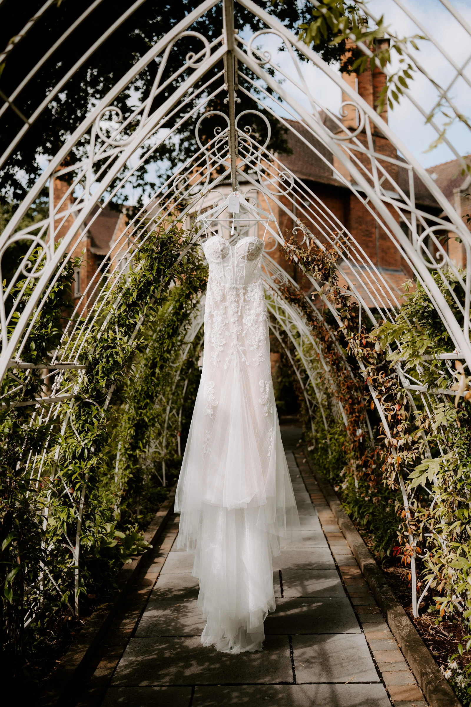 Emily’s wedding dress hanging beneath a garden arch at Moxhull Hall