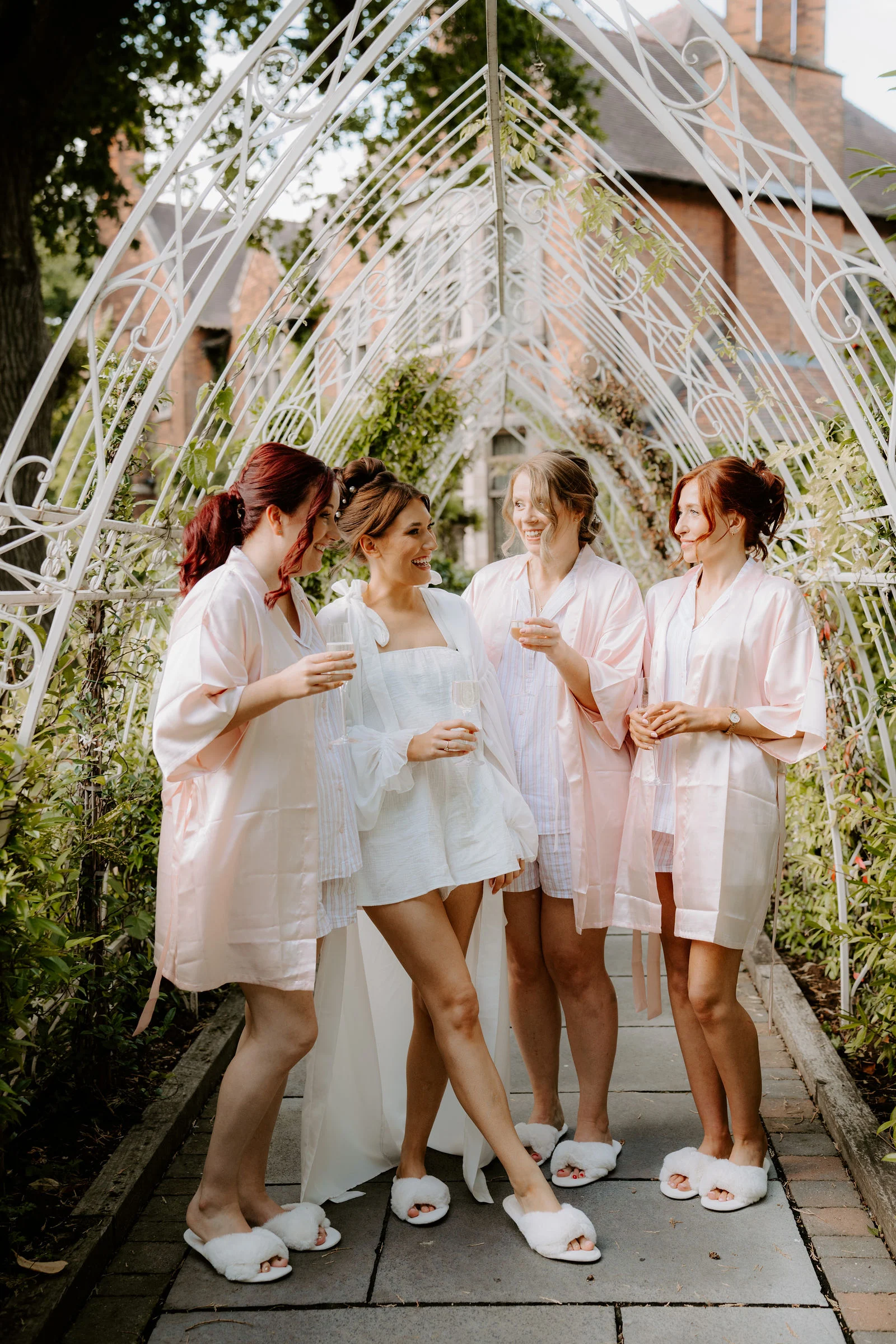 Emily and her bridesmaids laughing beneath a garden arch at Moxhull Hall