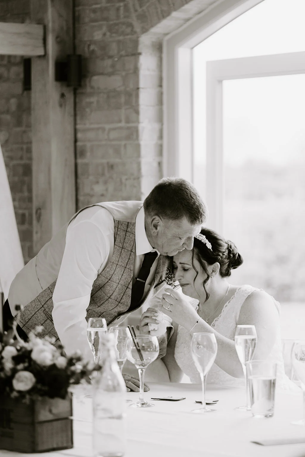 Sarah-Jane and James sharing a kiss beside their wedding breakfast table in black and white