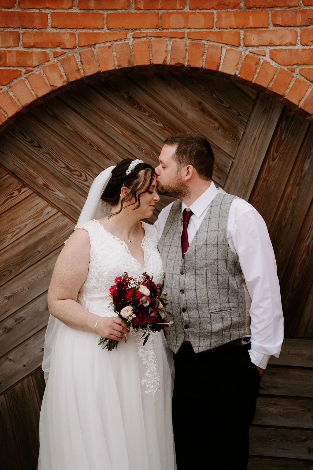 Sarah-Jane and James kissing in front of a brick arch and wooden doors