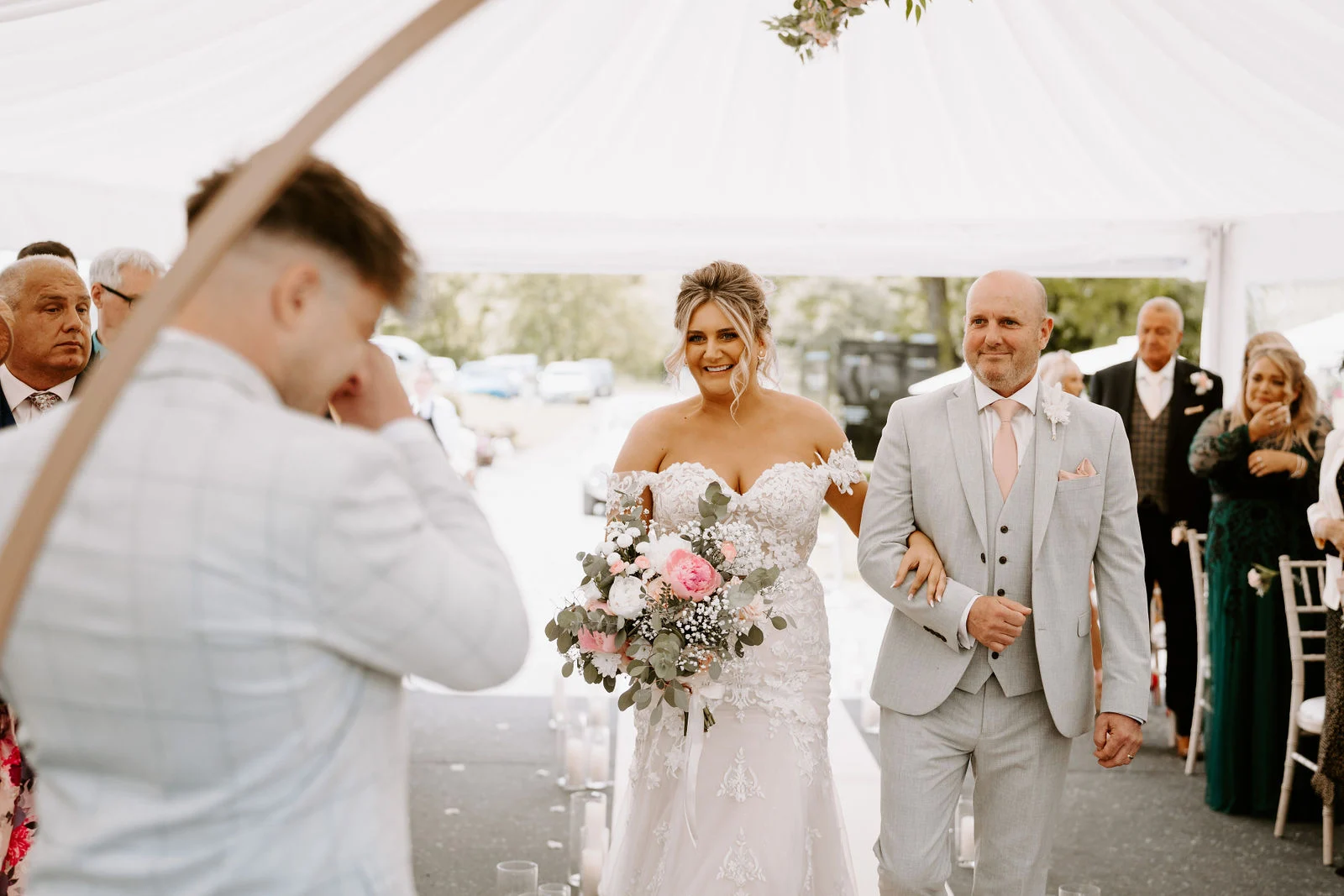 Bride walking down the outdoor aisle alongside her father toward the groom at Lakeside Venue