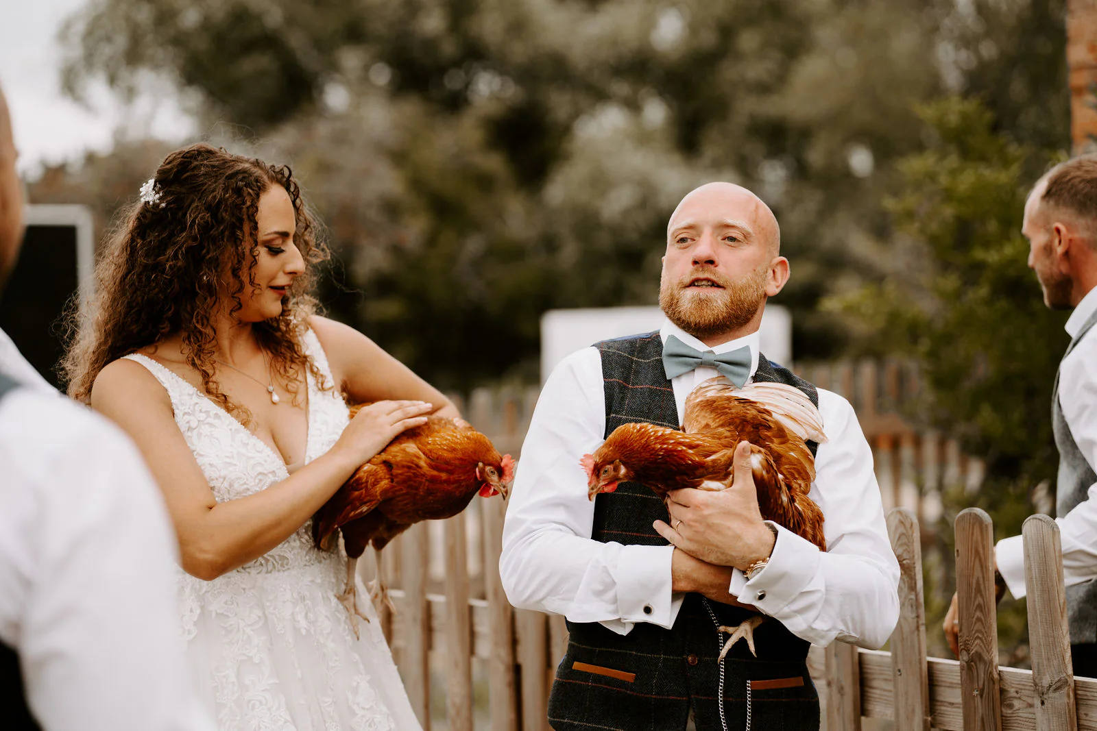 Kelly and Josh each hold a brown hen beside a wooden fence, laughing