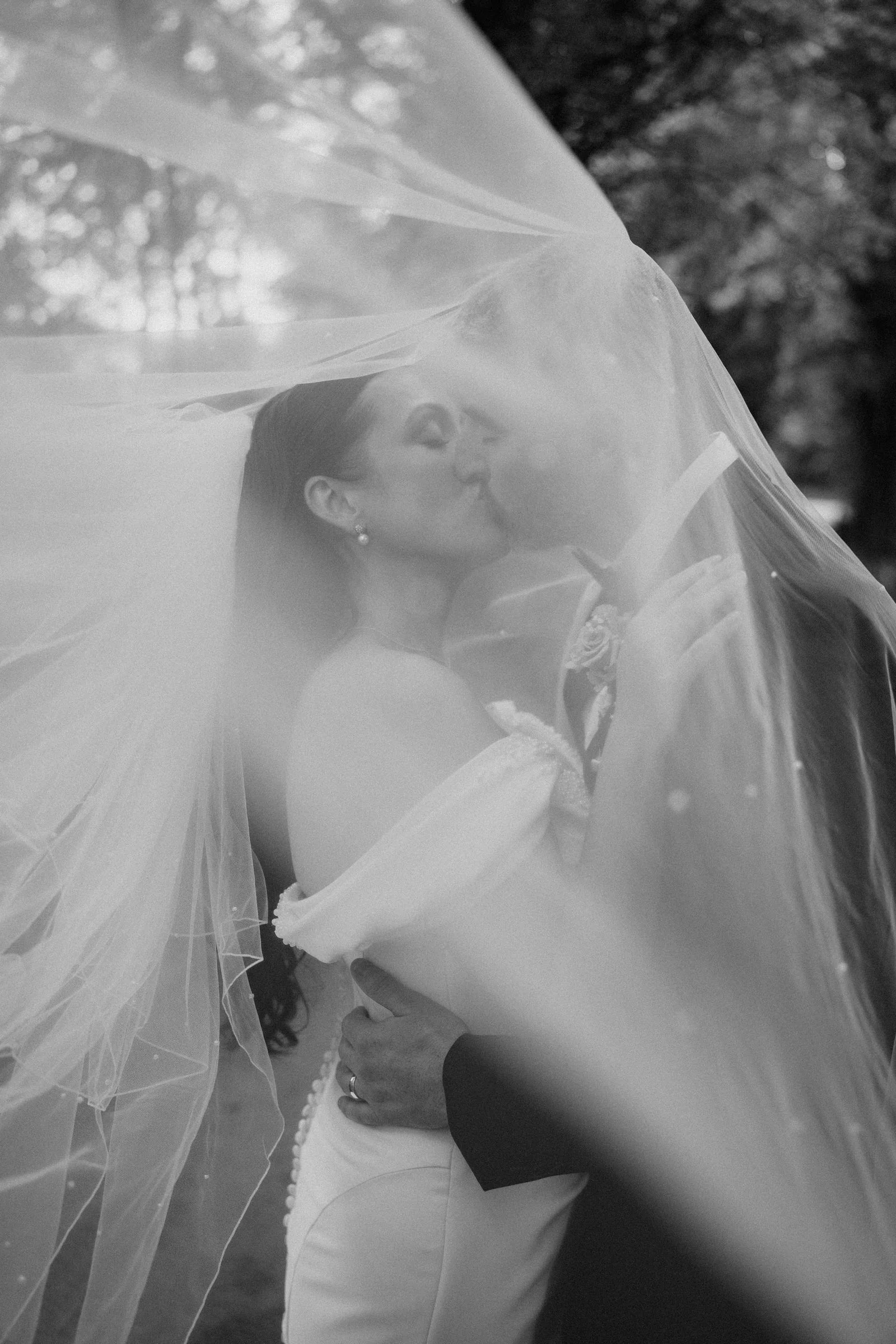 A black and white close portrait of the couple kissing beneath the bride's long veil