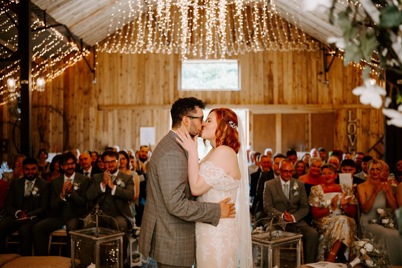 Georgia and Marcus kissing during their ceremony beneath the barn lights at Alcumlow Wedding Barn