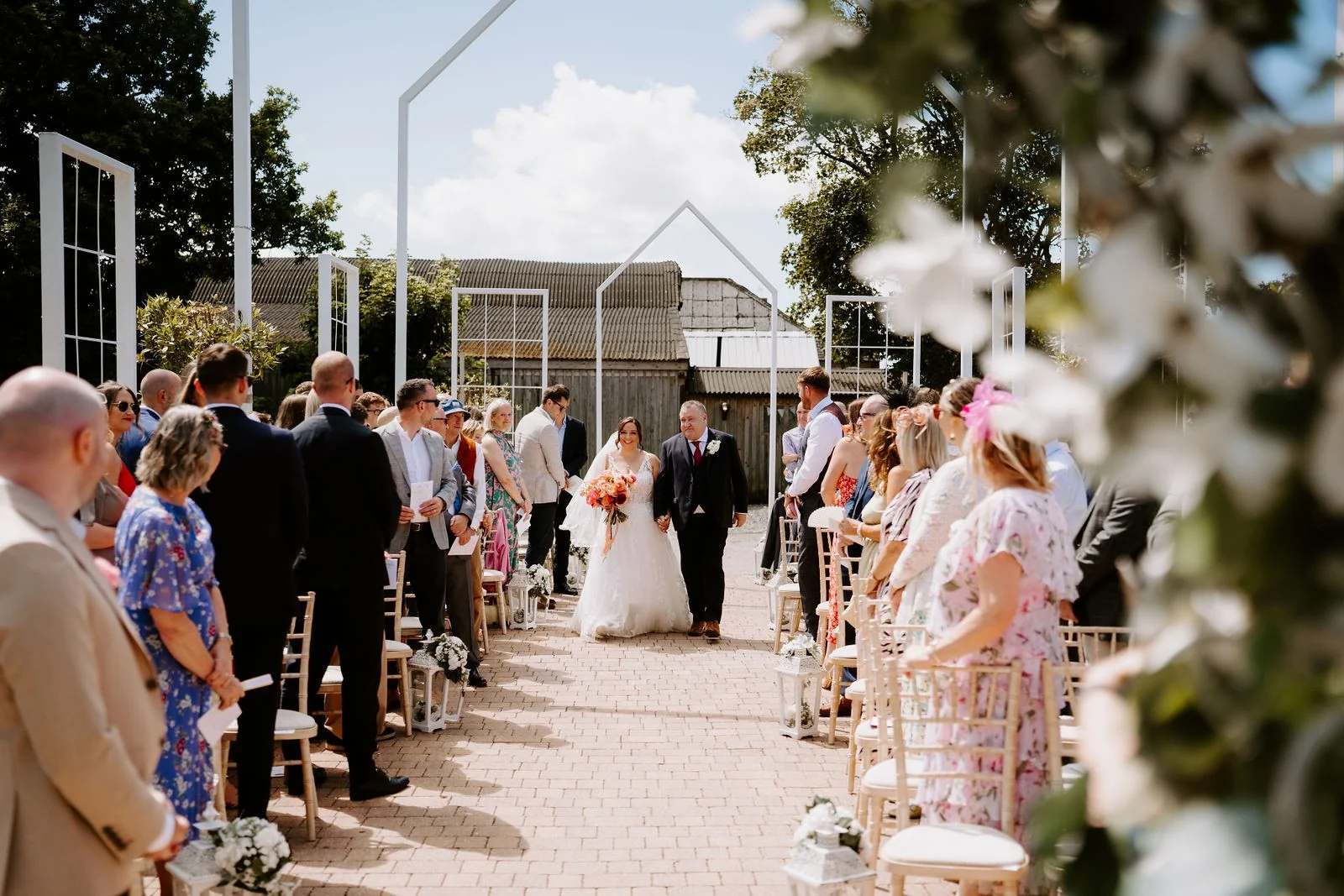 Lauren walking towards the outdoor ceremony with guests seated either side at Alcumlow Wedding Barn