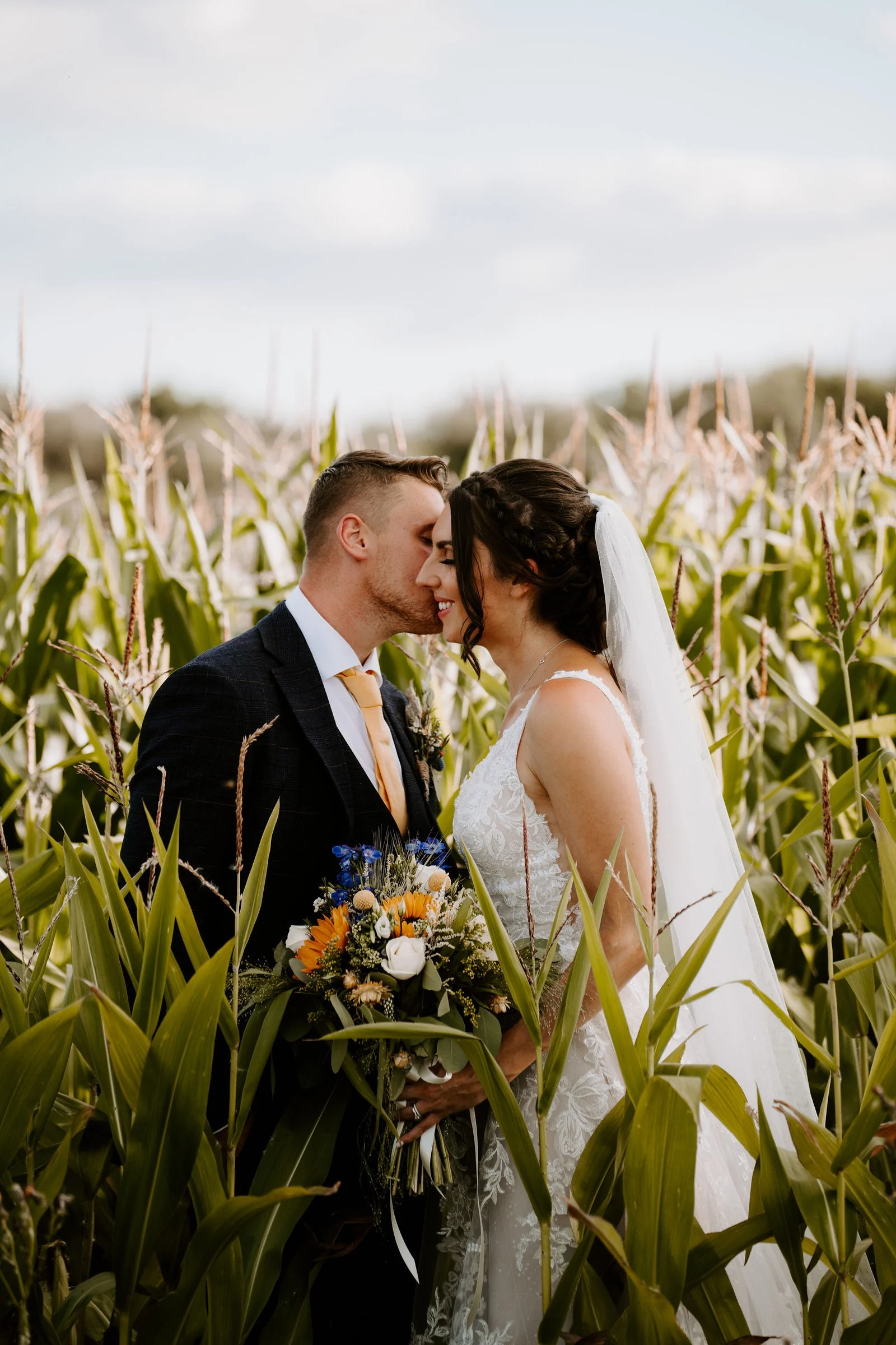 Martha and Harry kissing among the maize plants at Alcumlow Wedding Barn