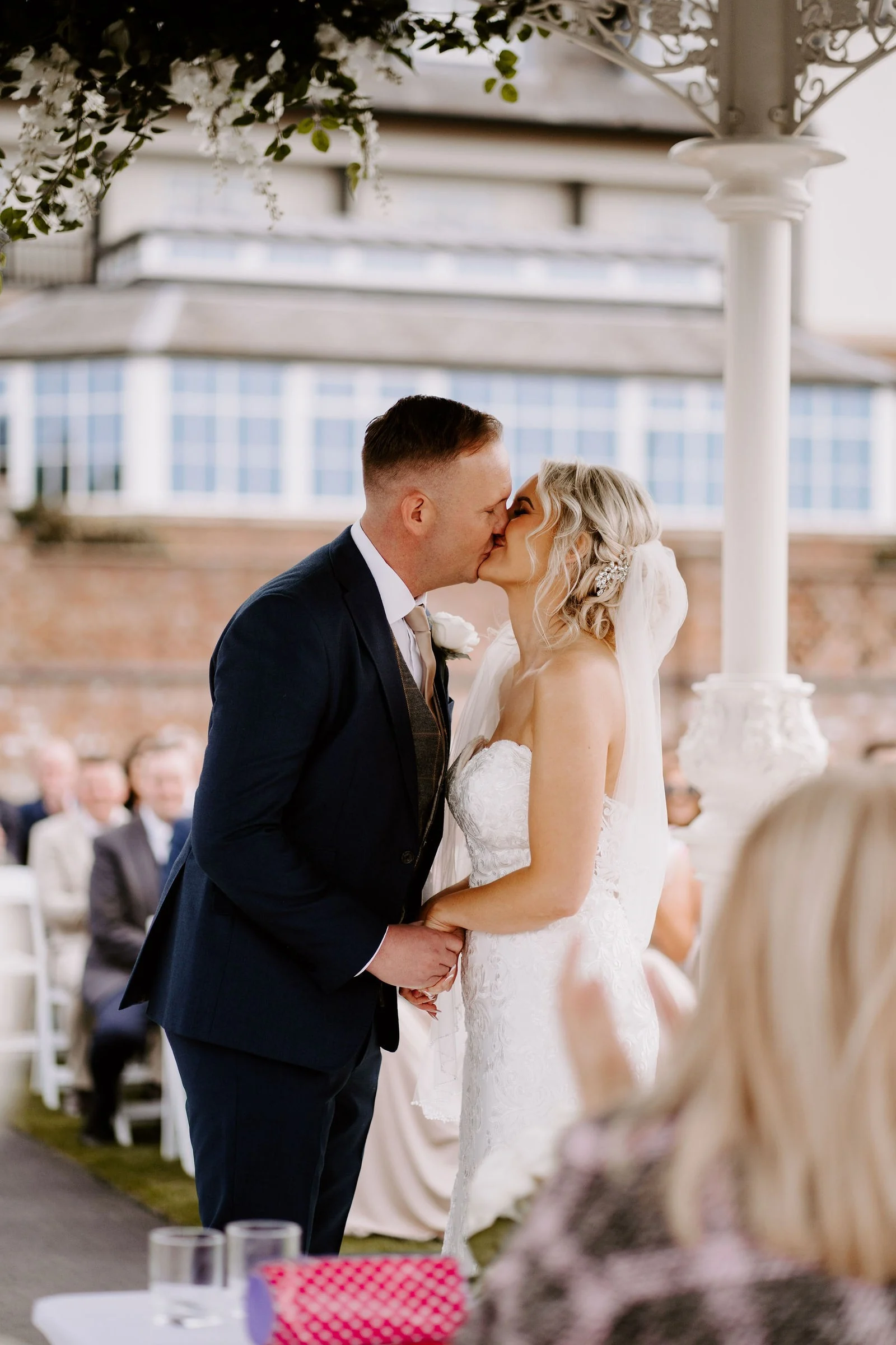 Emma and James kissing beneath the outdoor gazebo at Carden Park Hotel