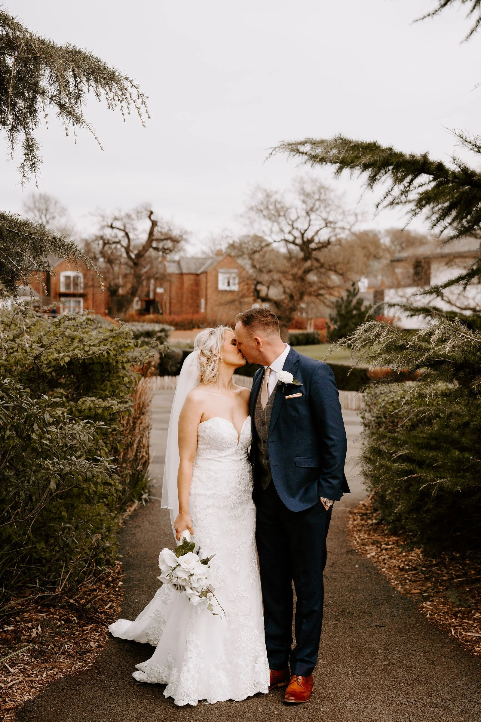 Emma and James sharing a kiss on a garden path at Carden Park Hotel