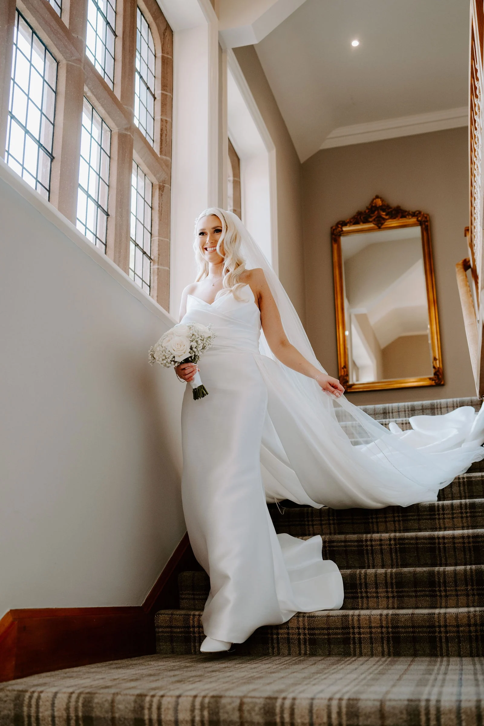 Hannah standing beside a tall window in her wedding dress at Colshaw Hall