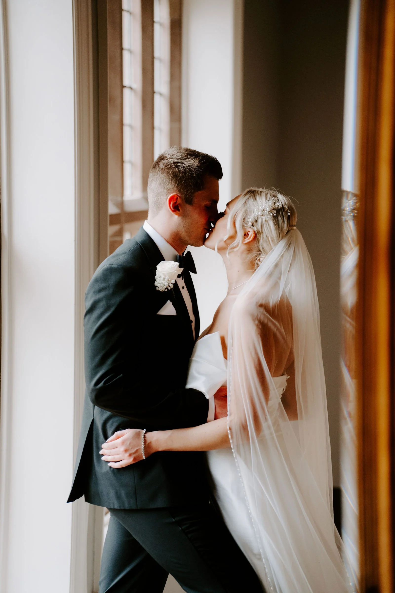 Hannah and Rob kissing beside a window at Colshaw Hall