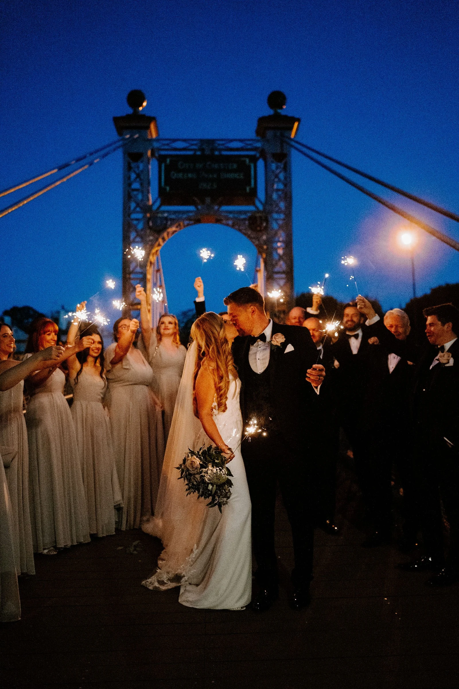 Chloe and John celebrating with sparklers beside Chester’s suspension bridge after dark