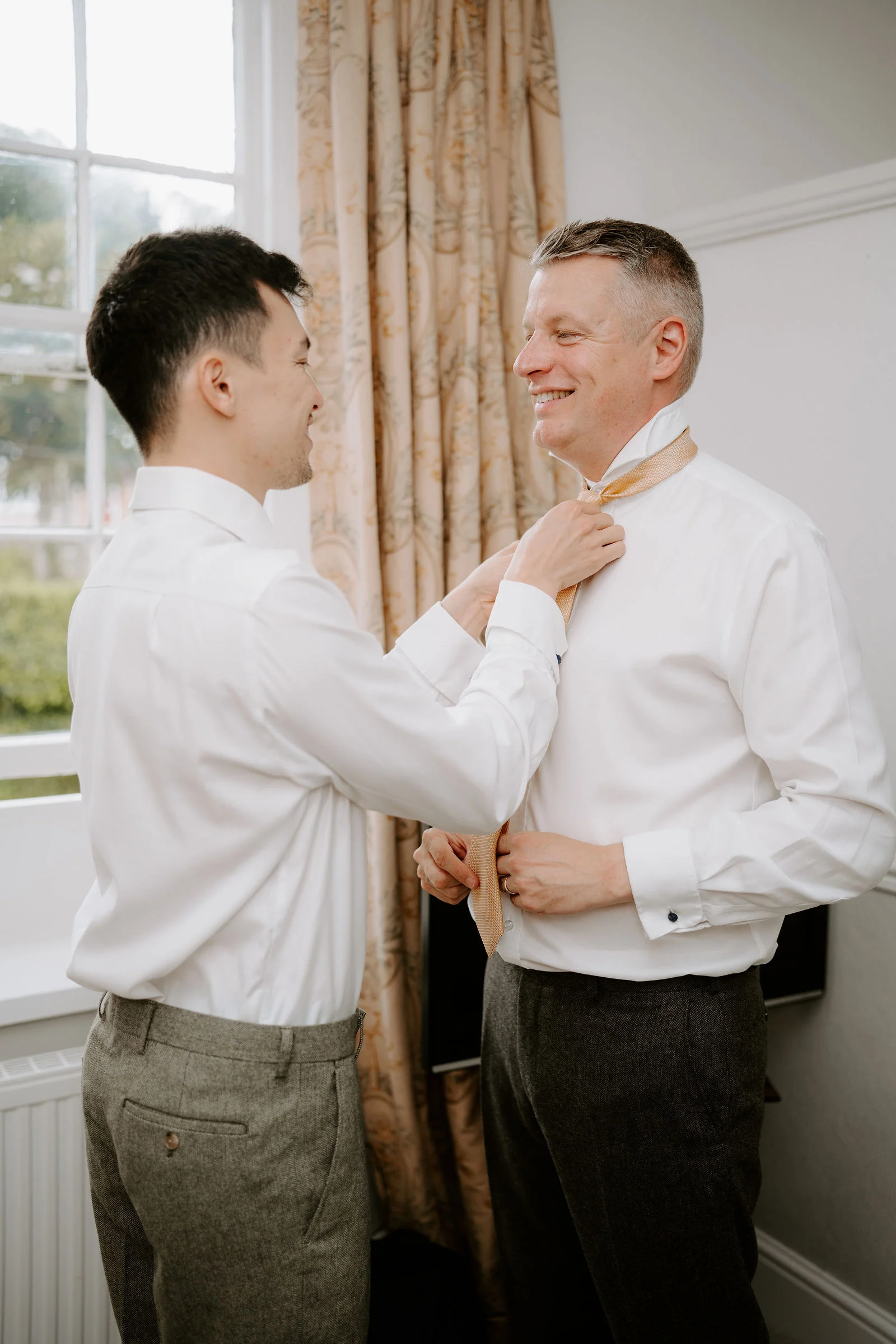 Groom fastening his tie during morning preparations at Port Eliot Estate