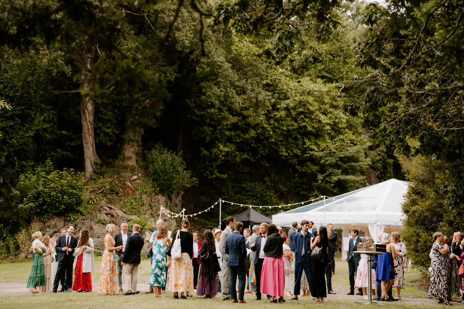 Wedding guests mingling on the estate lawn outside the grand marquee during drinks reception at Port Eliot Estate