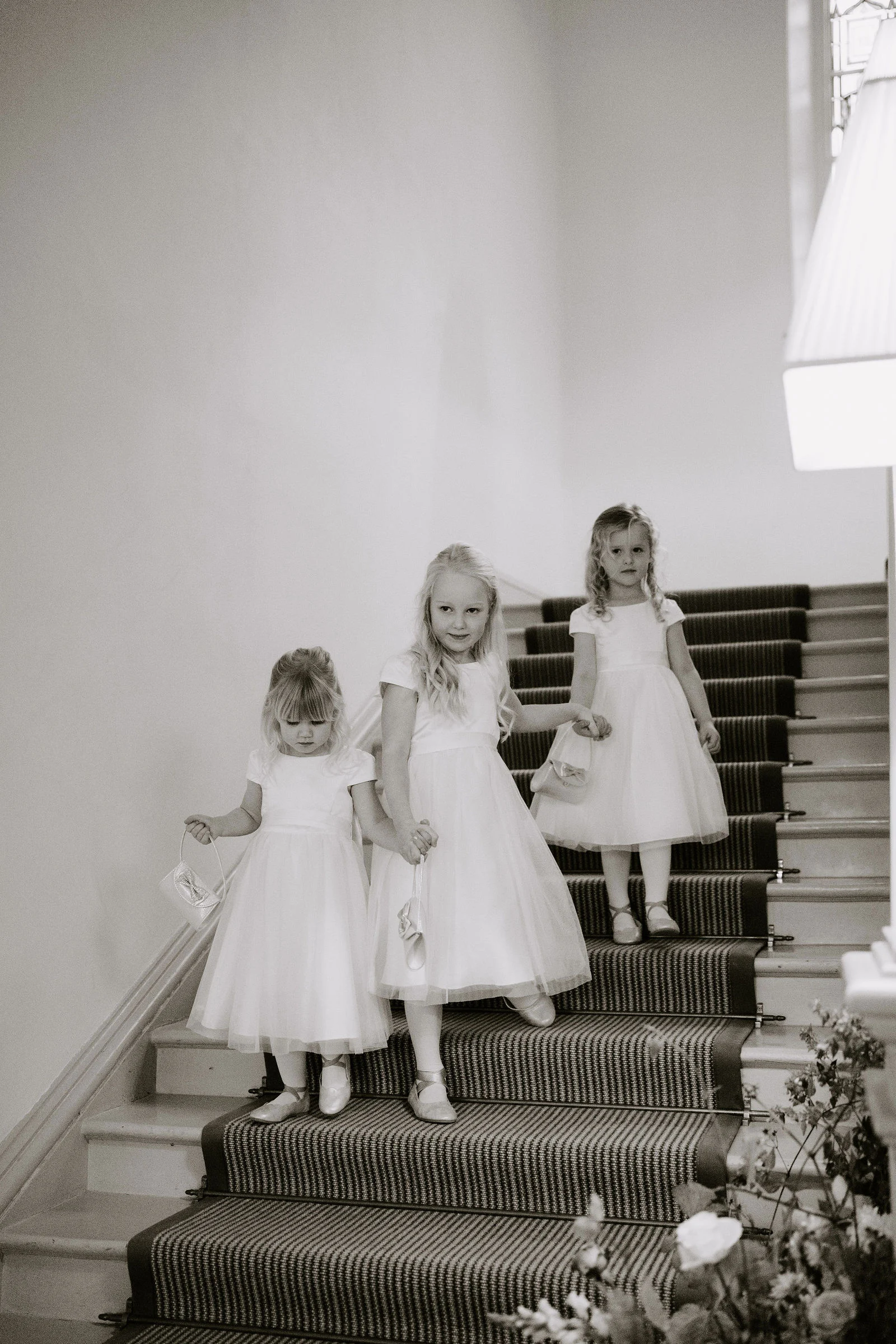 Black and white portrait of flower girls descending the grand cantilevered staircase at Pynes House