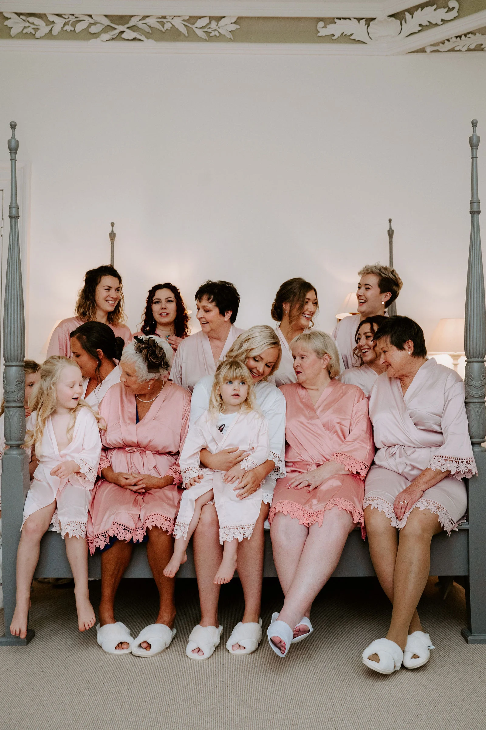 Bridal party laughing together in matching pink robes on the four-poster bed at Pynes House