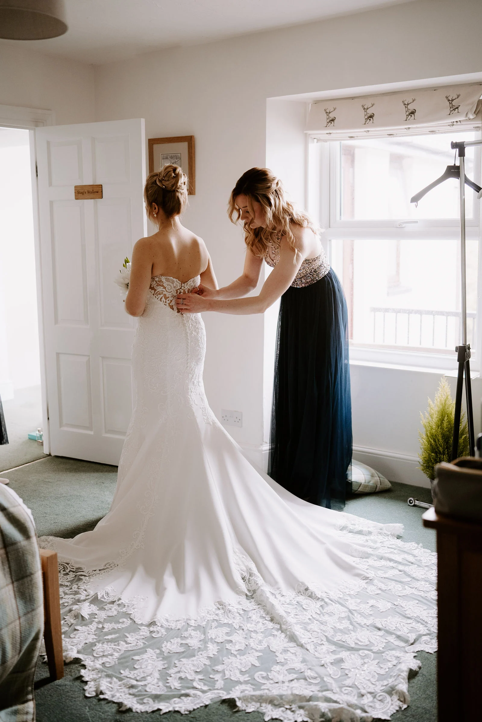 Bridal prep moments with bridesmaids fastening the wedding dress overlooking the sea at Sandy Cove Hotel