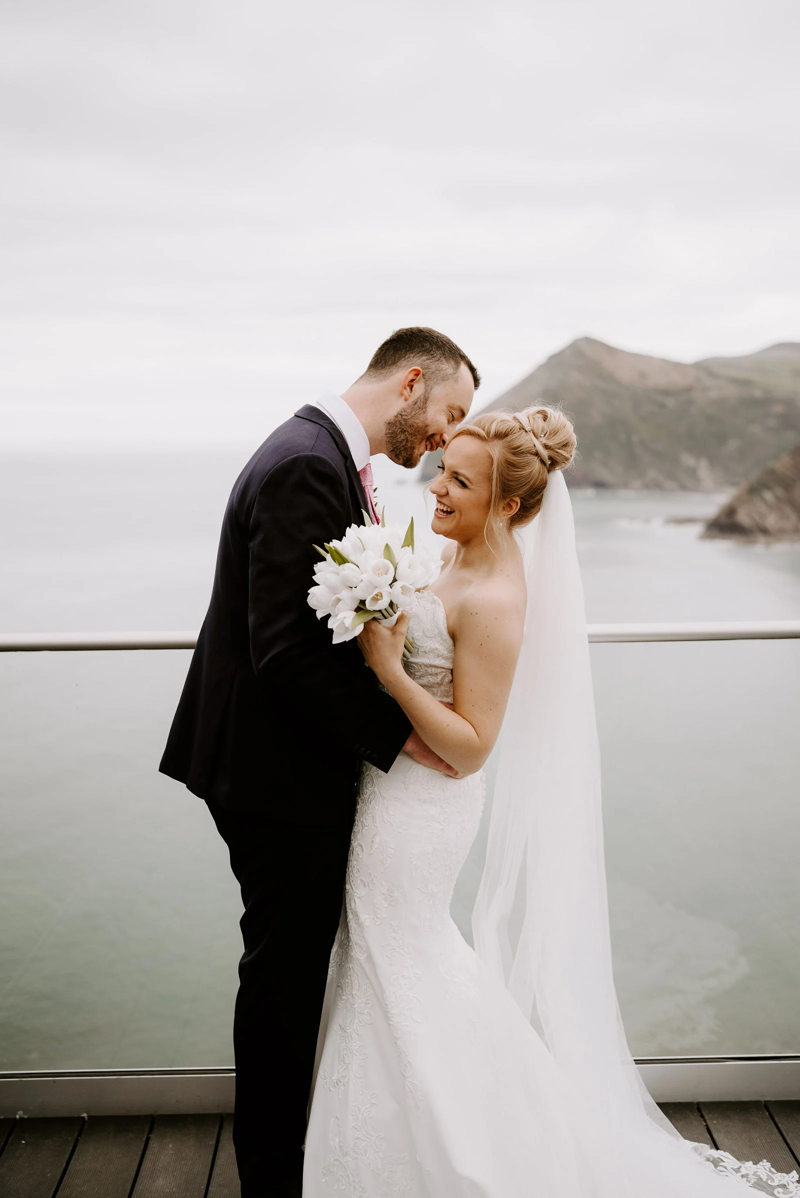 Gareth and Georgina embracing on the dramatic clifftop headland overlooking the sea at Sandy Cove Hotel
