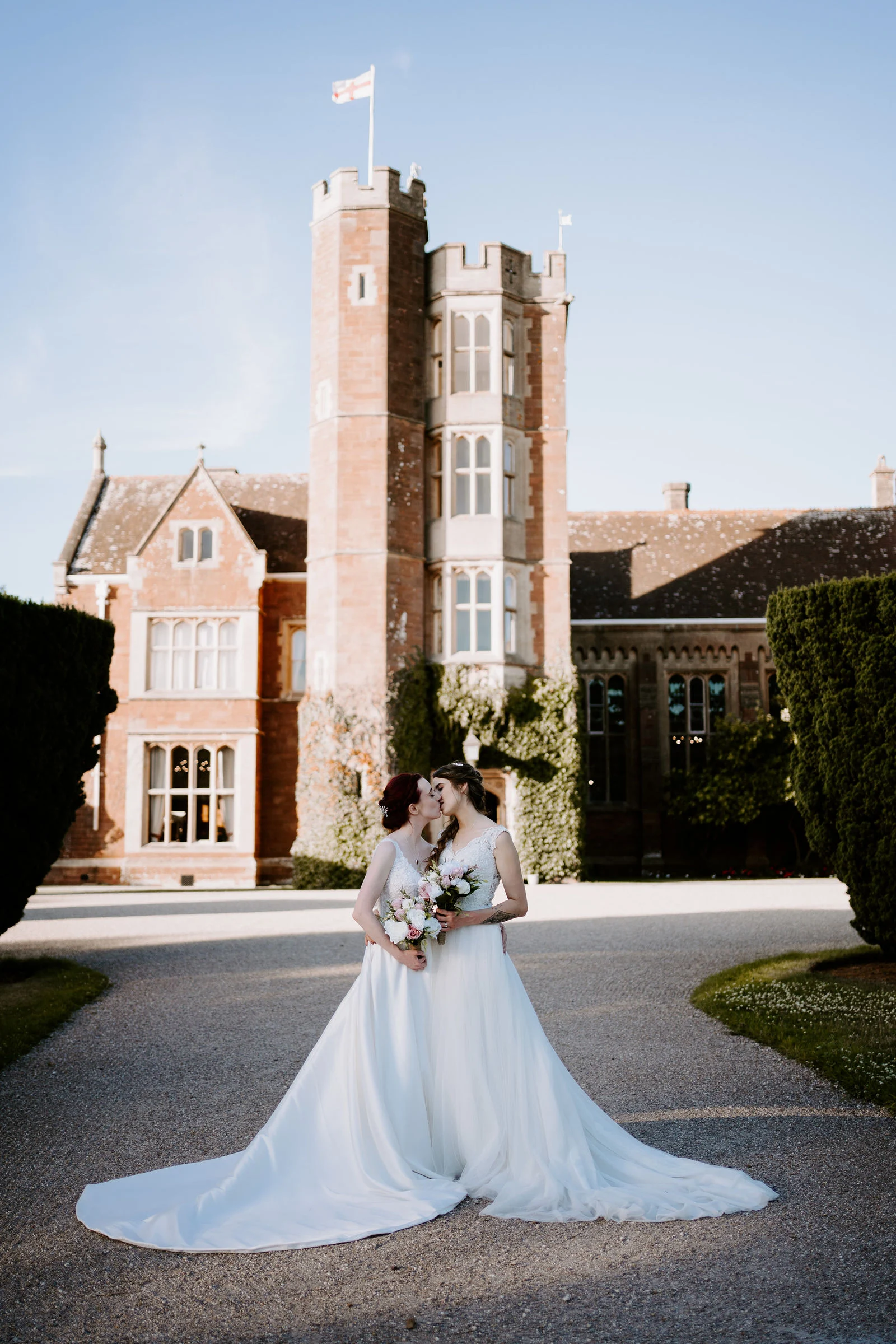 Jodie and Natalie sharing a romantic kiss in front of the historic stone manor house tower at St Audries Park
