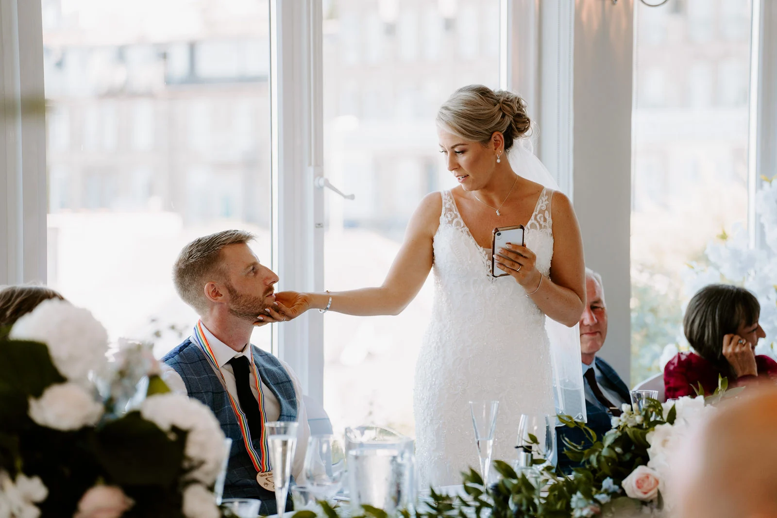Sarah delivering a heartfelt speech at the banquet table gently touching Rob's chin during wedding breakfast