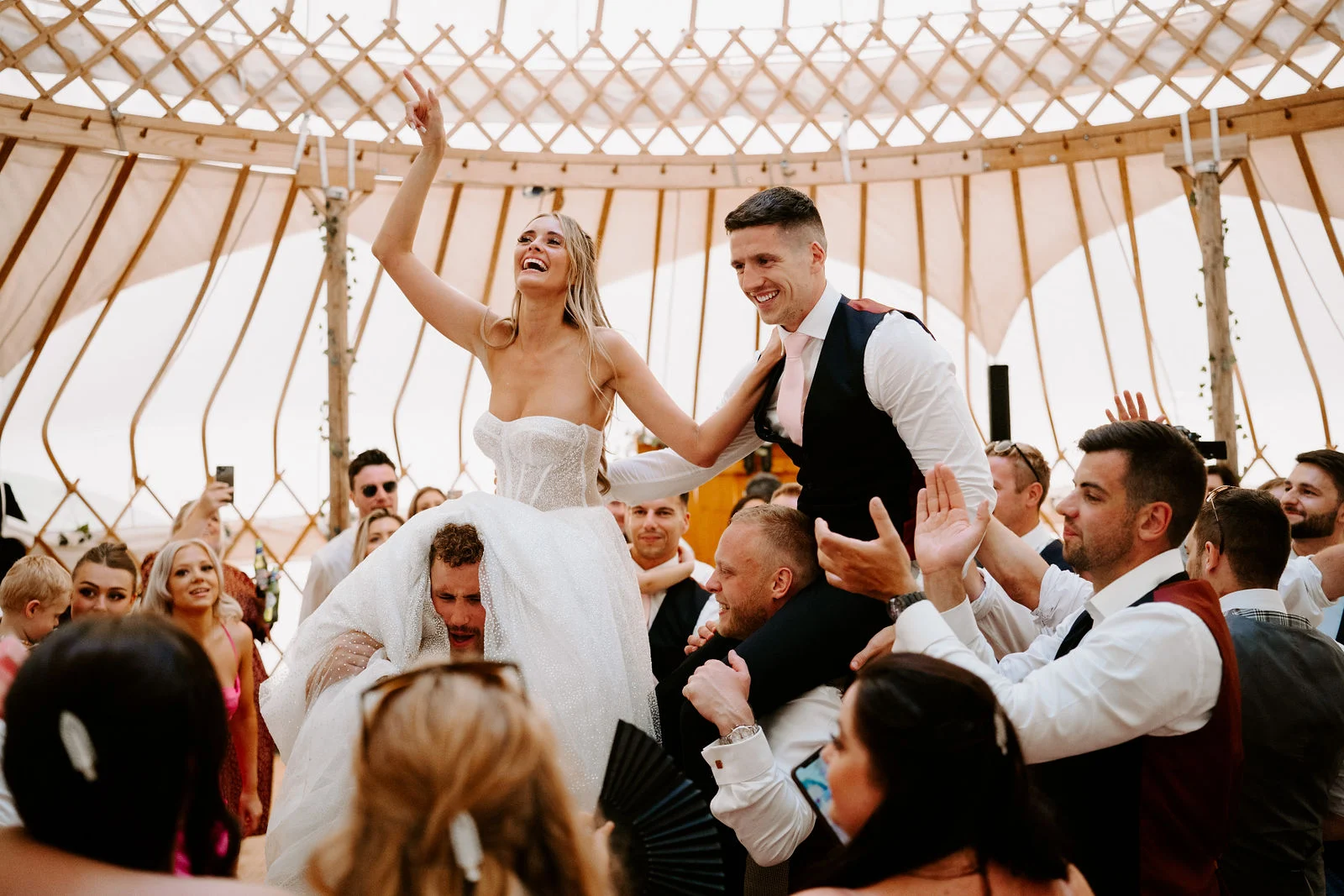 Maria and Dom lifted onto friends' shoulders during an energetic festival wedding party inside the rustic timber barn at Whitemoor Farm