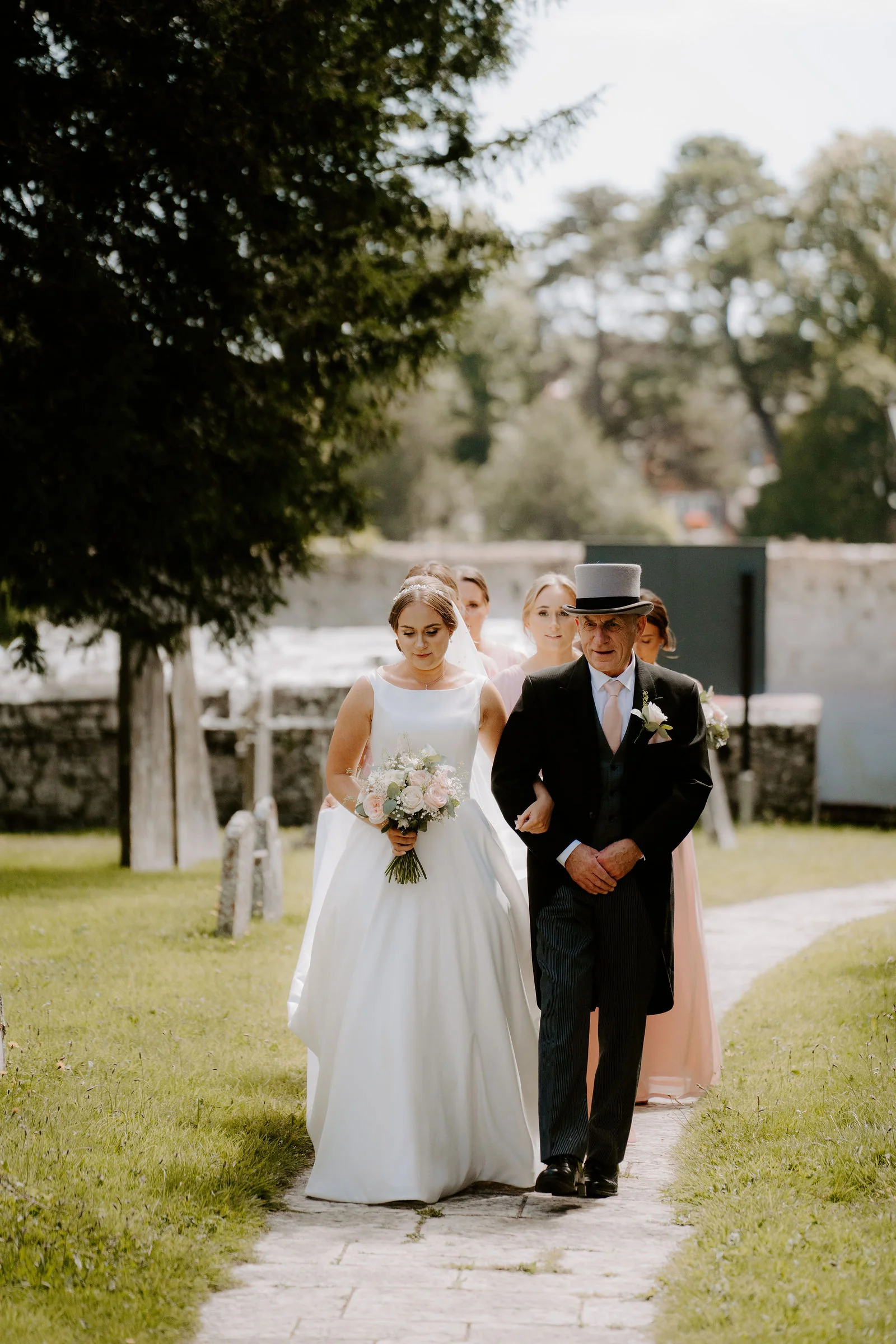 Chloe walking arm in arm towards the church with bridesmaids behind her