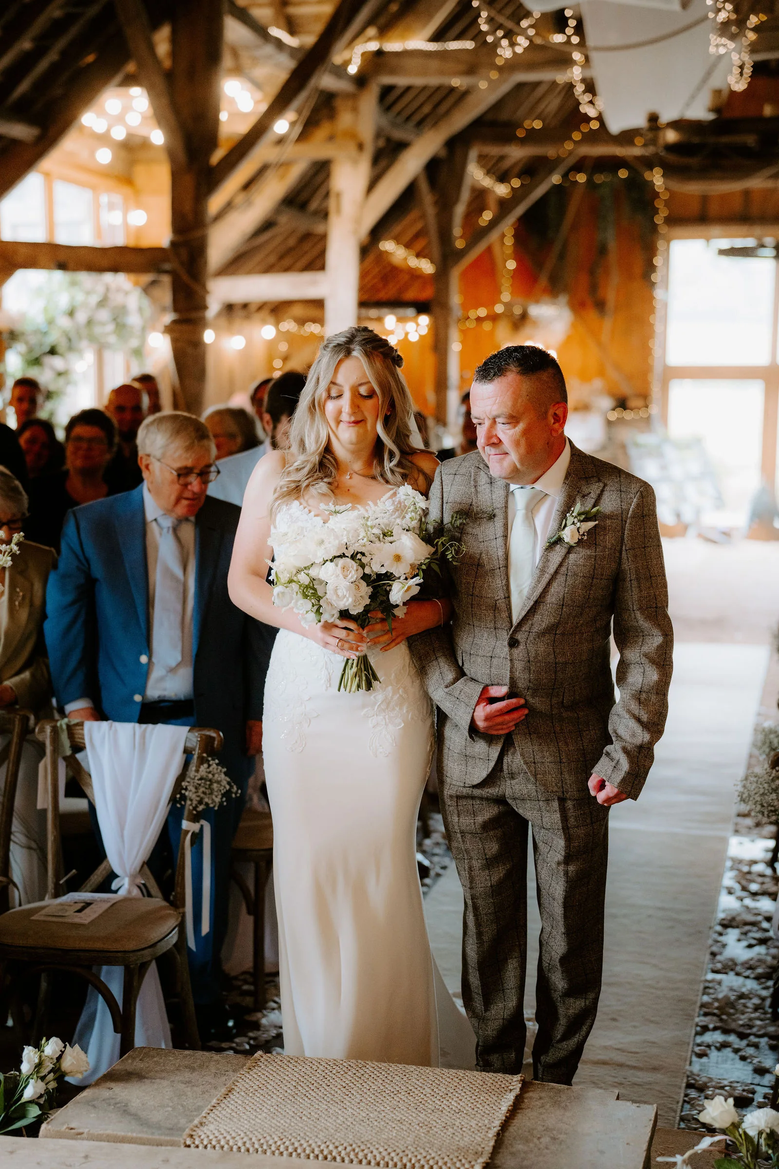 Amy walking down the aisle with her father inside the thatched barn at Bowerchalke