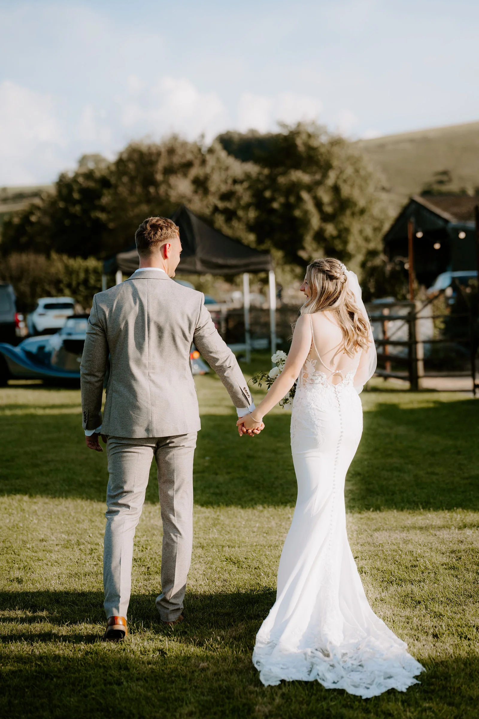 Edward and Amy walking hand in hand across the lawn with the thatched barn behind at Bowerchalke