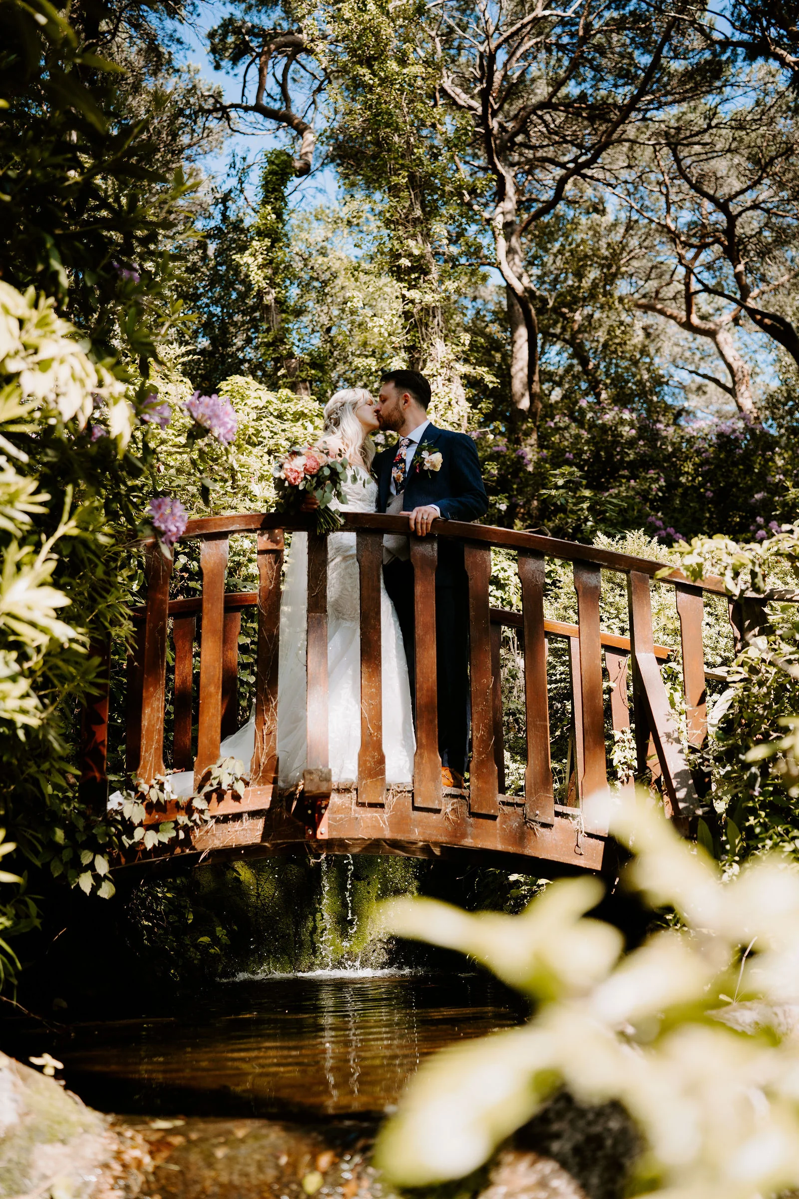 Erica and Pete kissing on a wooden bridge in the gardens of The Italian Villa