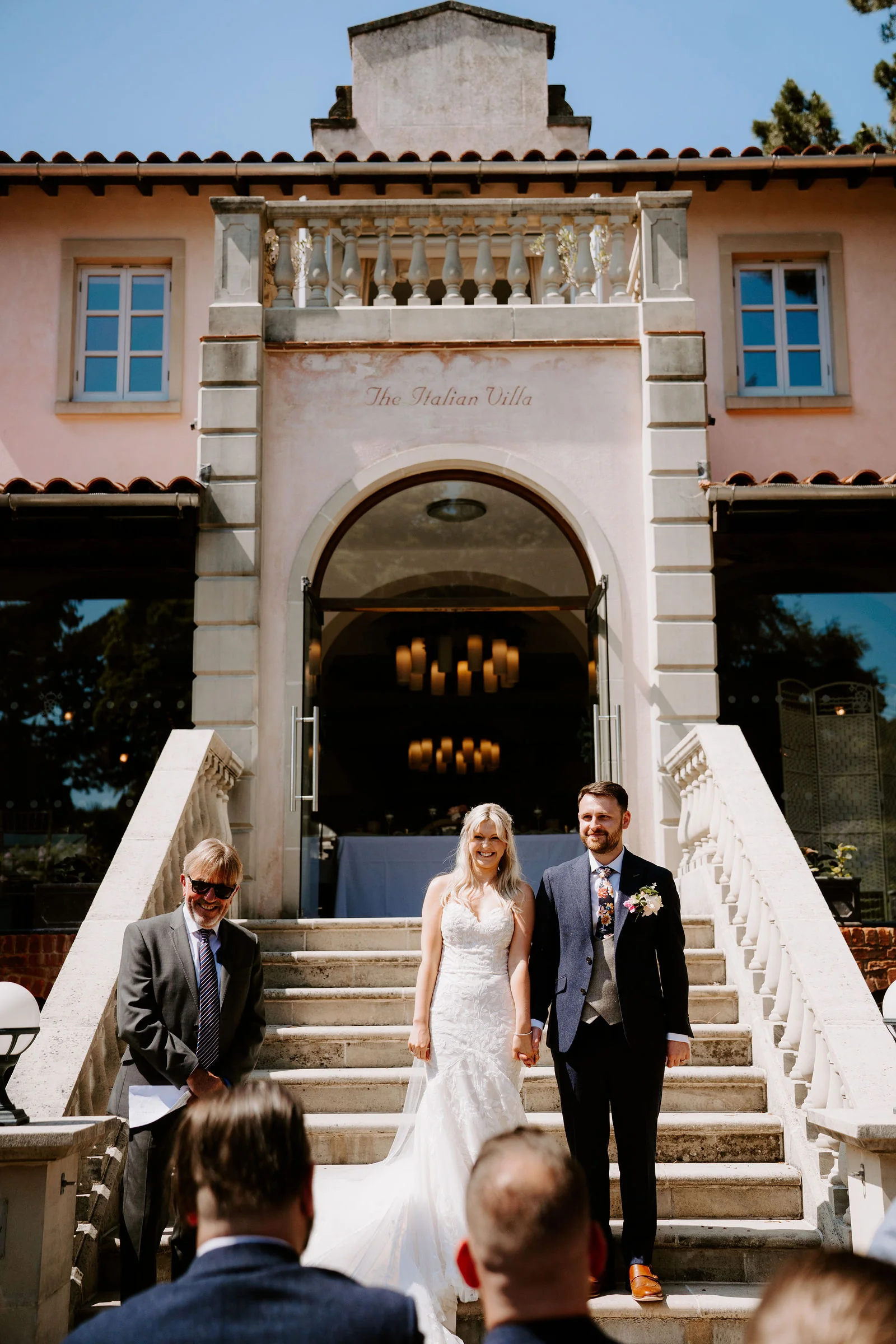 Erica and Pete holding hands and smiling on the entrance steps of The Italian Villa