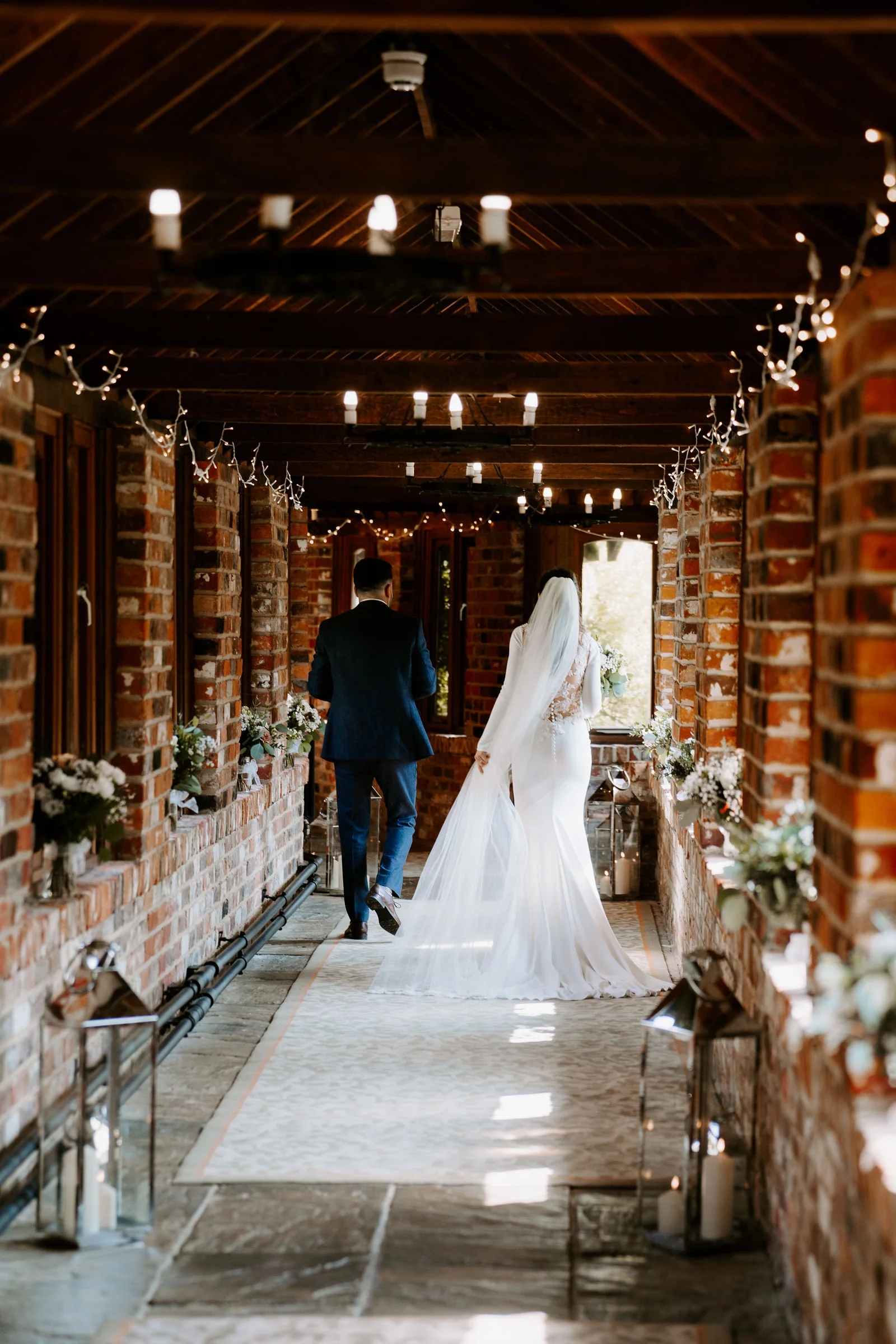 Hannah and Jamie walking hand in hand down the fairy lit brick cloister at Lainston House