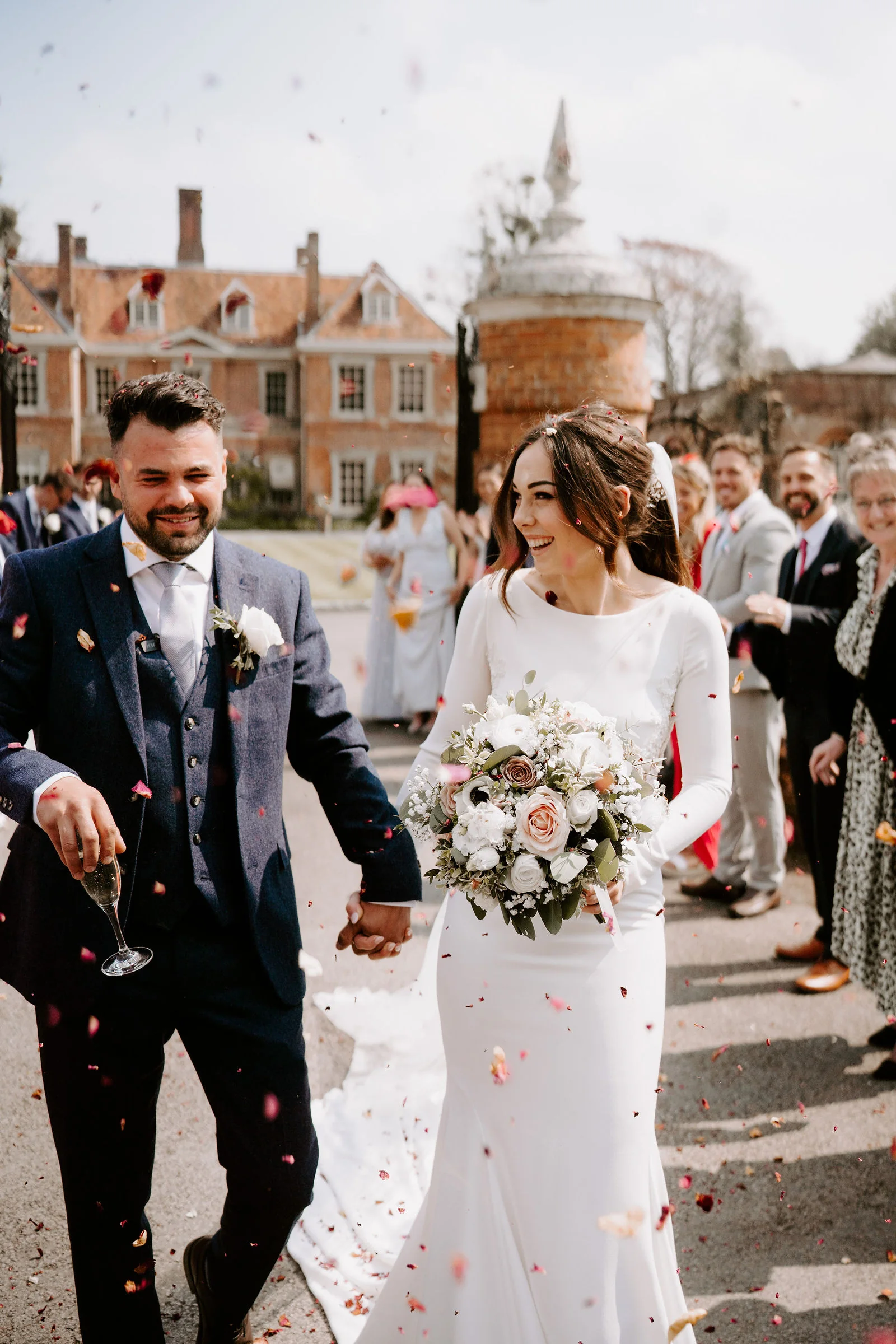 Hannah and Jamie walking through falling confetti with Lainston House behind them
