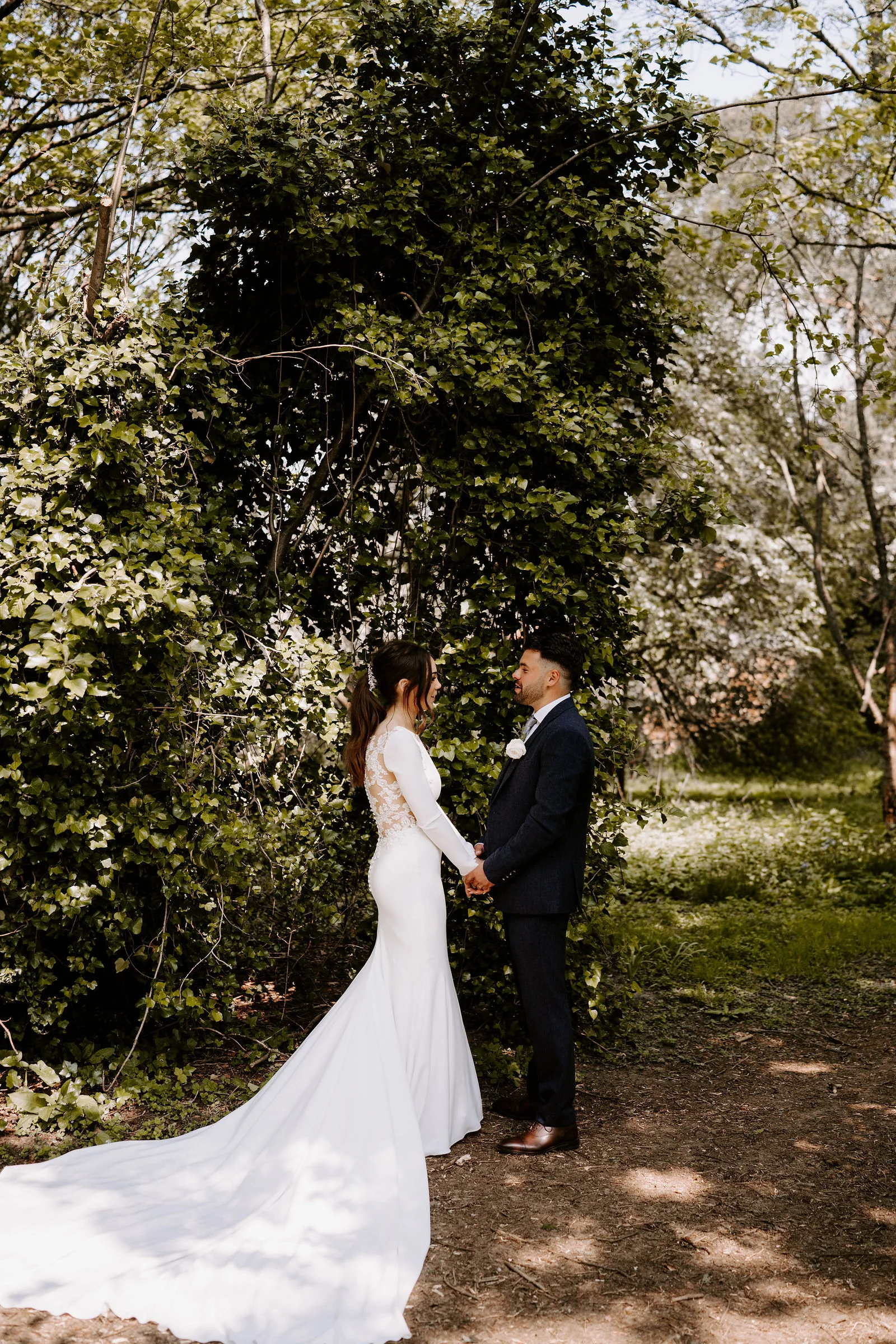 Hannah and Jamie holding hands before an ivy covered wall in dappled sunlight at Lainston House