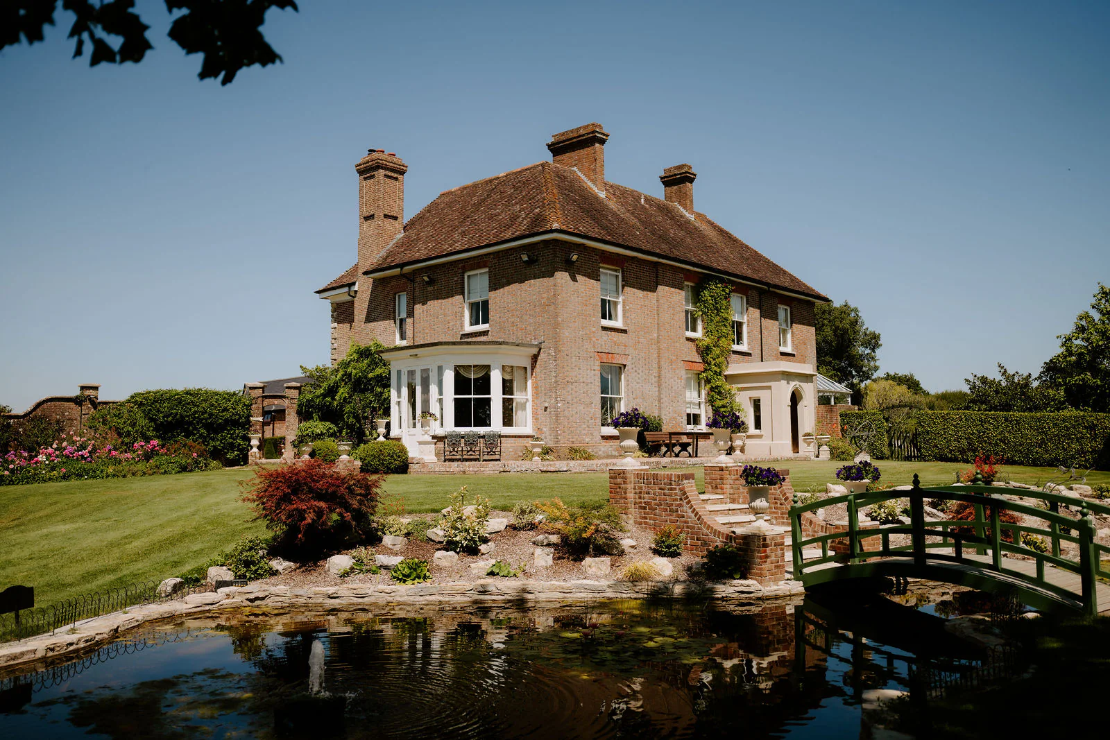 A small wooden bridge over a pond in front of the manor house at Parley Manor in summer