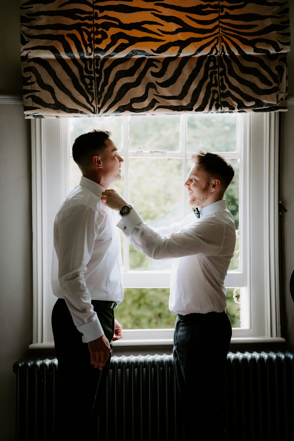 Ryan having his bow tie adjusted beside a window before the wedding