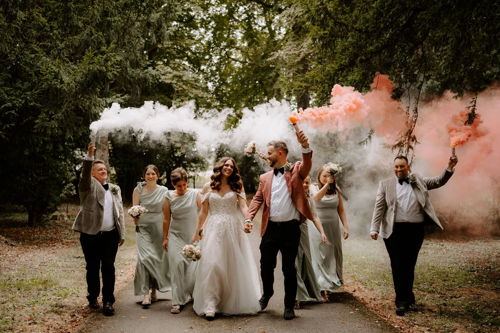 James and Laressa with their wedding party and pink smoke beneath the trees