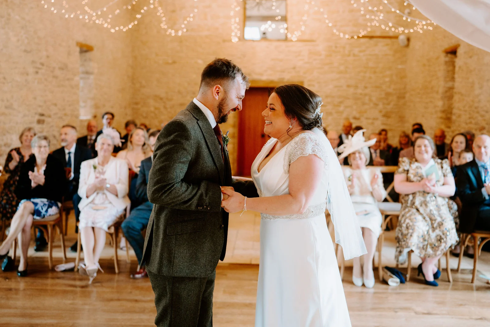 Zoe and Jack exchanging vows inside the vaulted stone threshing barn at The Kingscote Barn in Gloucestershire