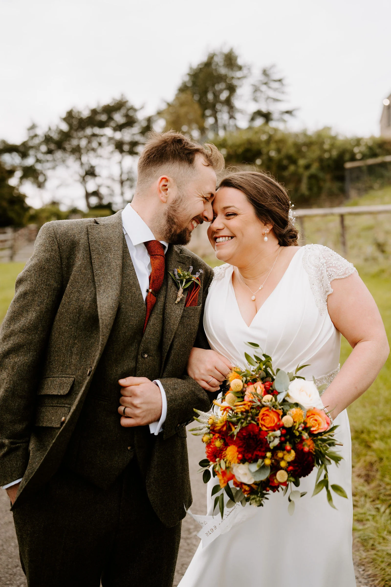 Zoe and Jack smiling together outside on the Cotswold stone courtyard at The Kingscote Barn