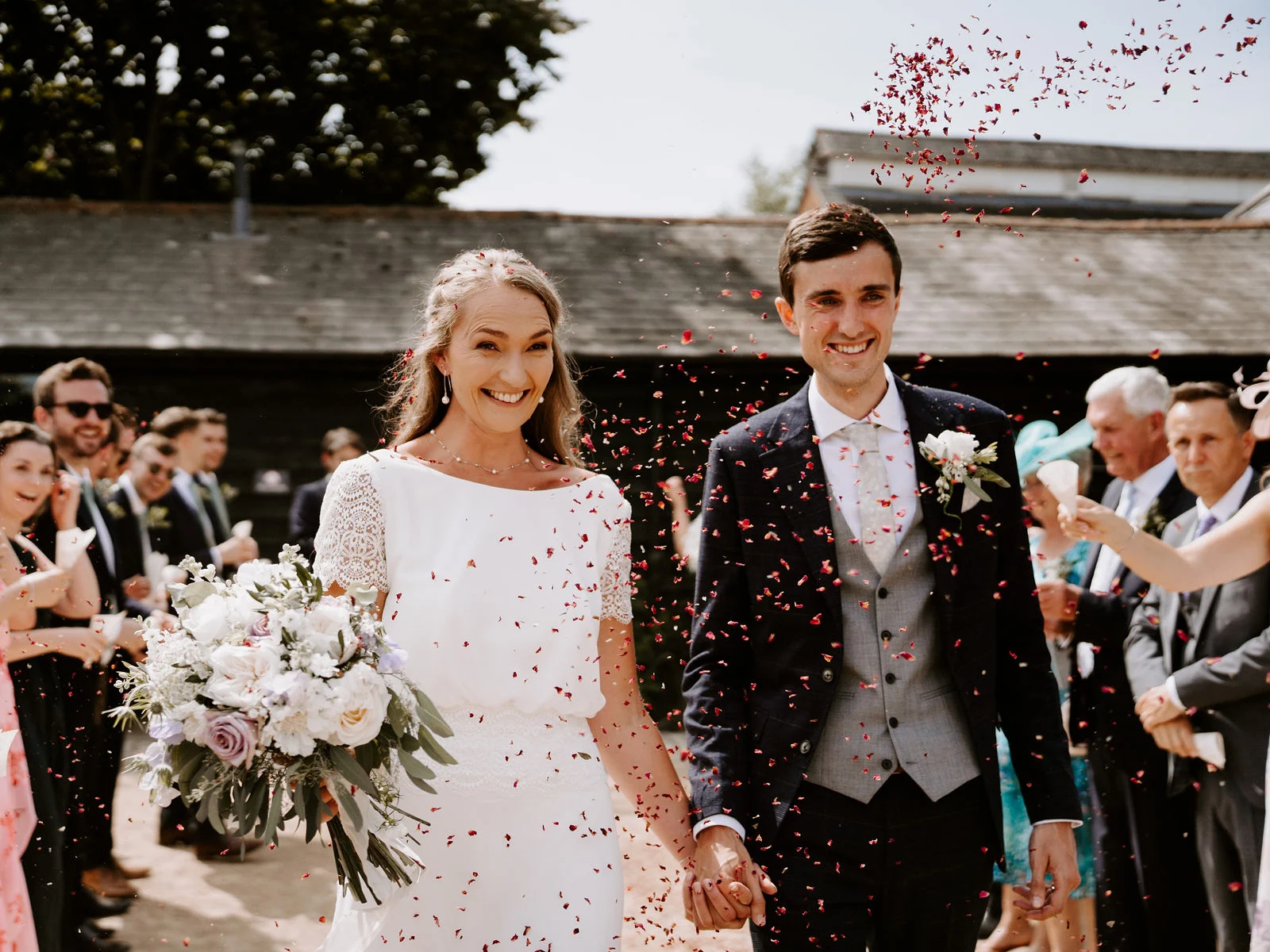 Tom and Sarah laughing beneath falling confetti after their Bury Court ceremony