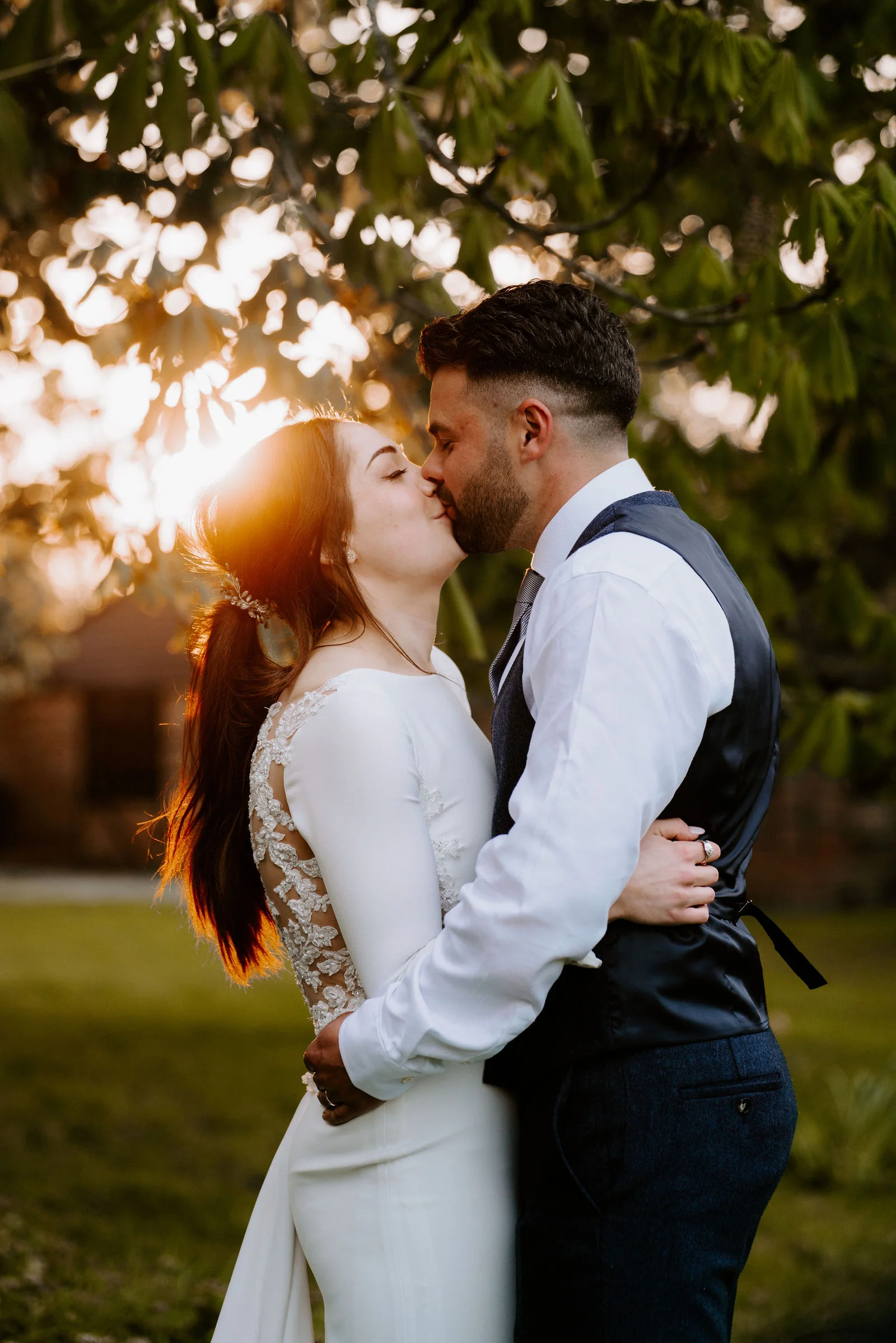 A bride and groom kiss in the golden light of the setting sun with the leaves of a tree glowing behind them at Lainston House