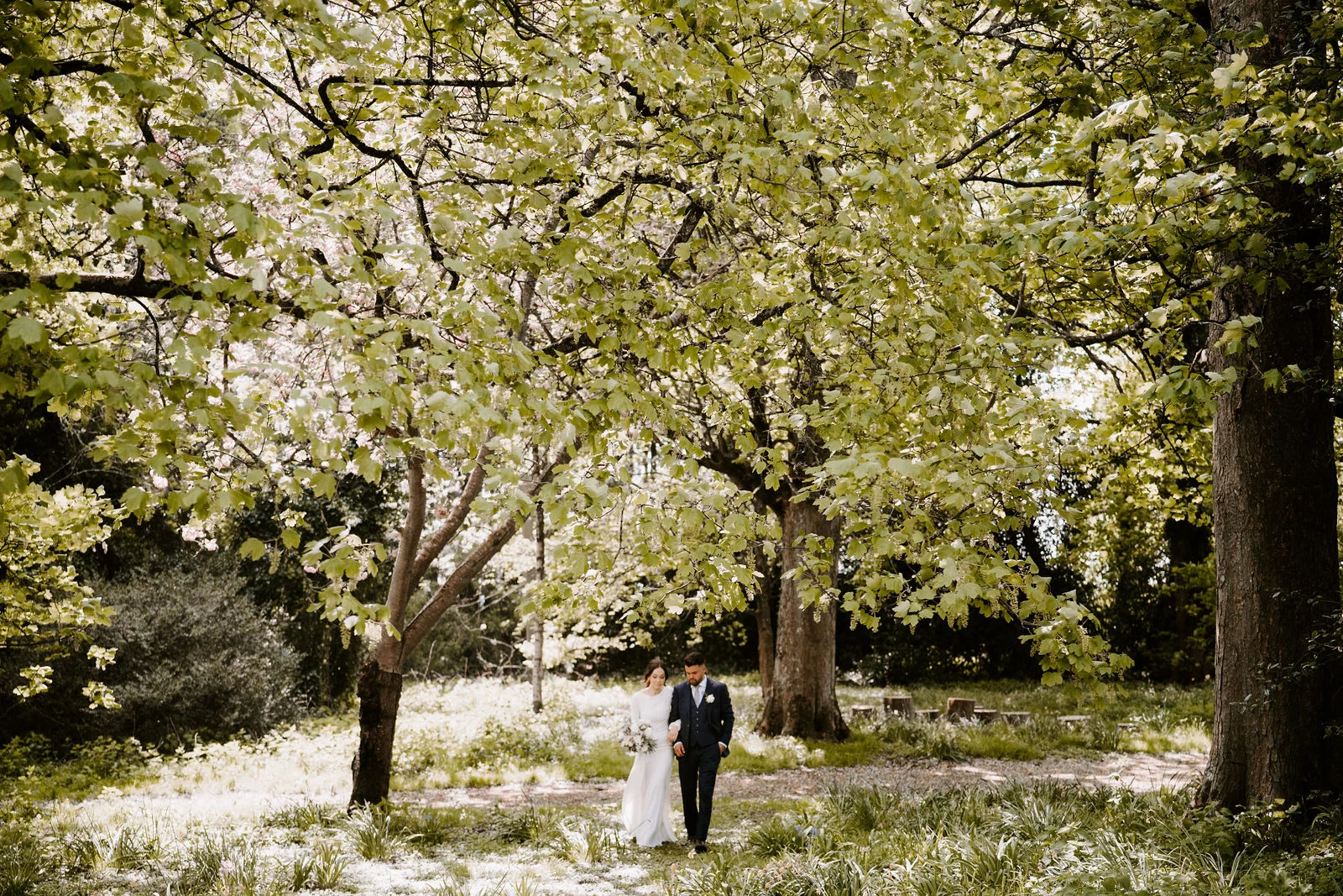 Hannah and Jamie walking beneath spring blossom in the grounds of Lainston House