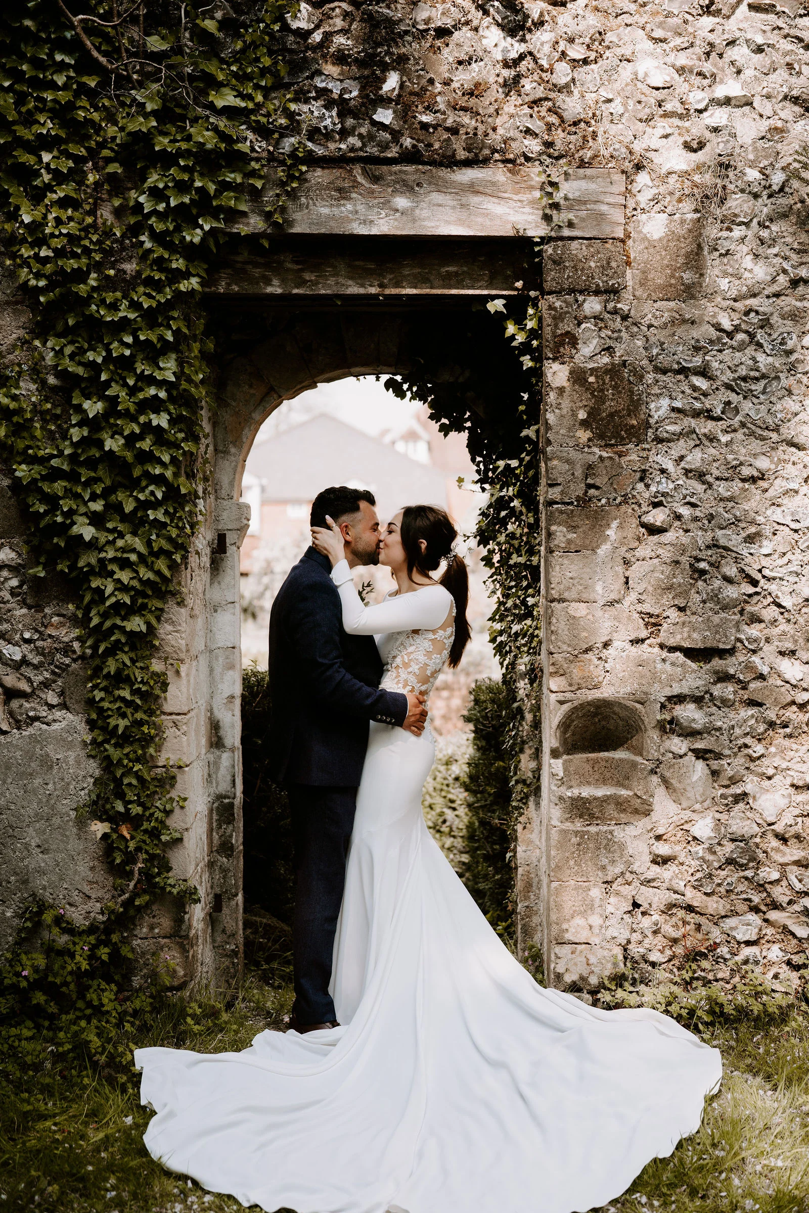 Hannah and Jamie sharing a kiss beneath an old stone arch at Lainston House