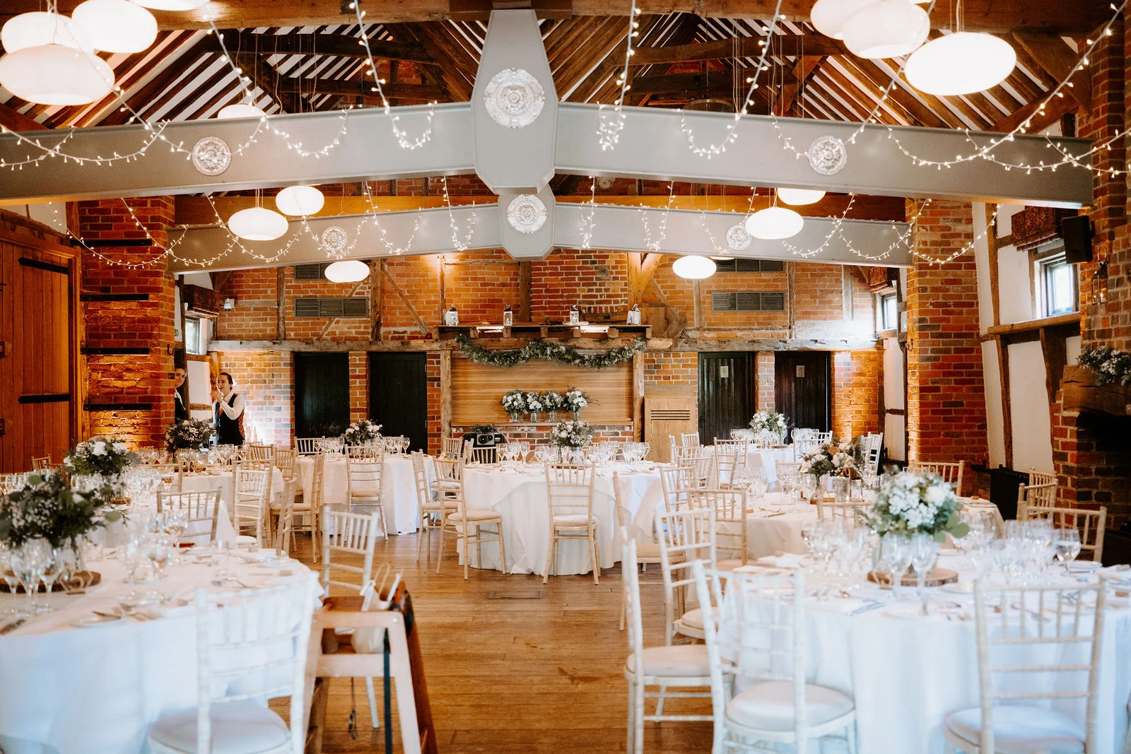Wedding breakfast tables beneath timber beams and white lanterns at Lainston House