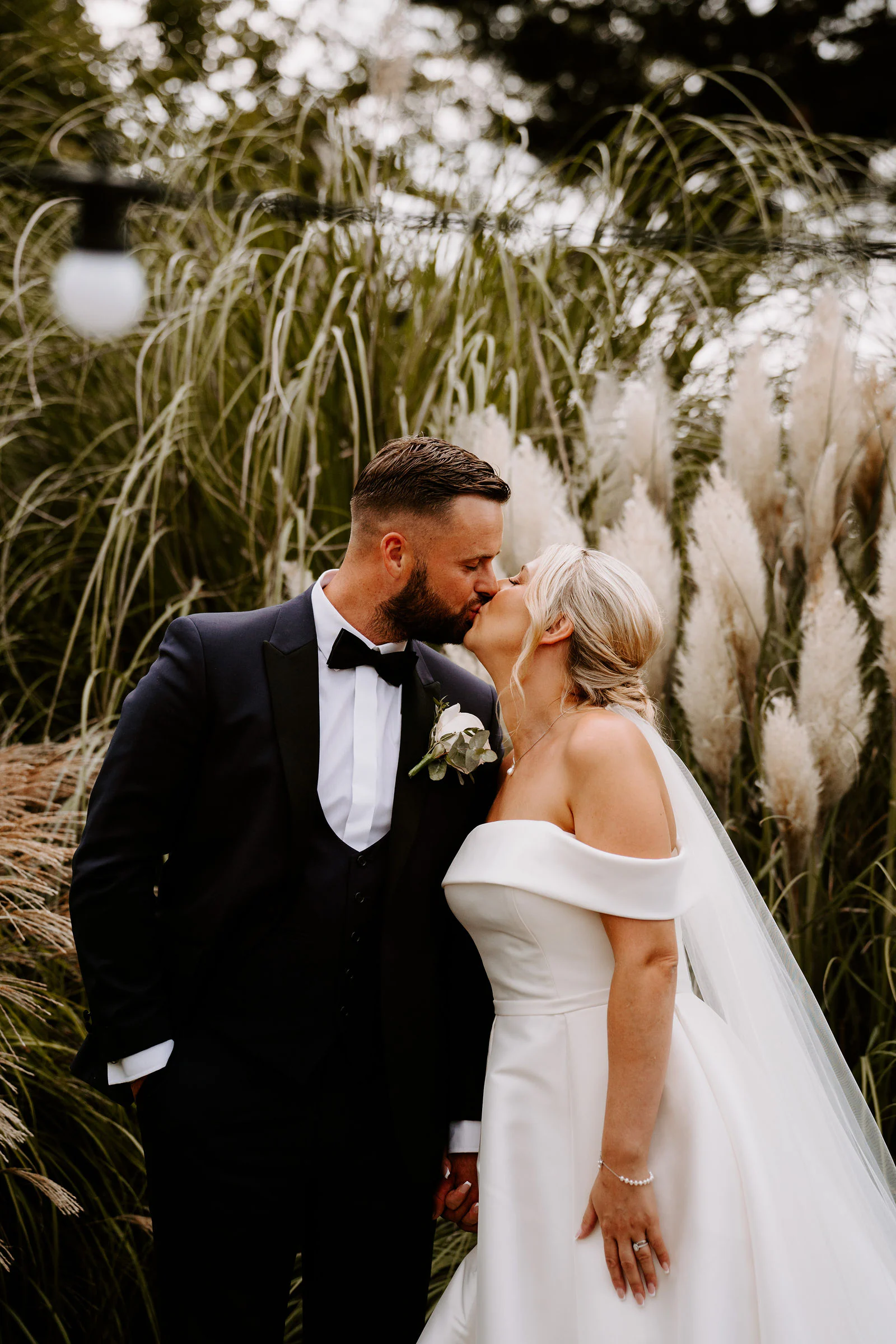 A bride and groom kiss among tall pampas grass at Hayne House in Hythe