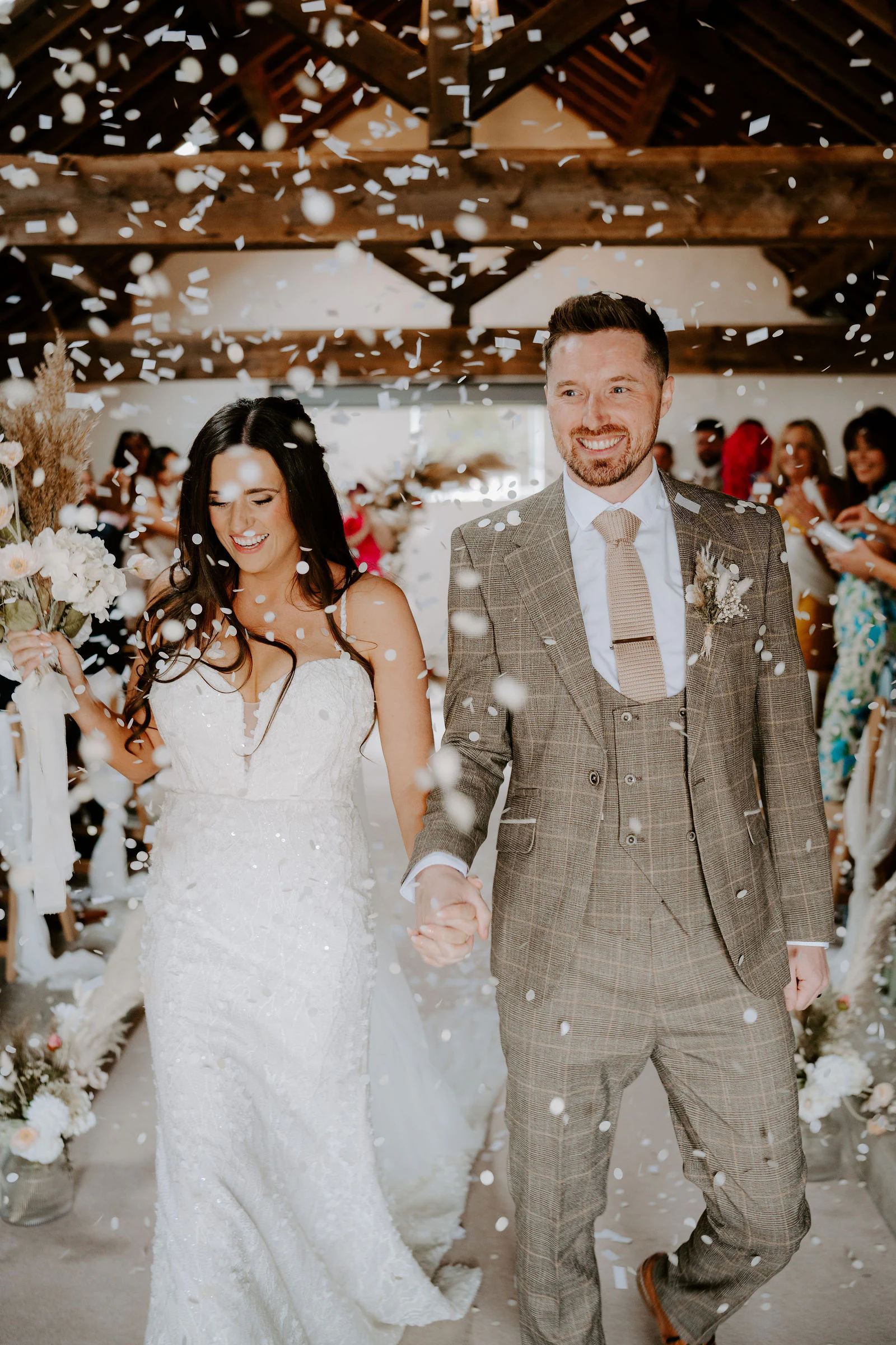 A bride and groom walk hand in hand through confetti down the aisle at Fairbank Barn in Staveley
