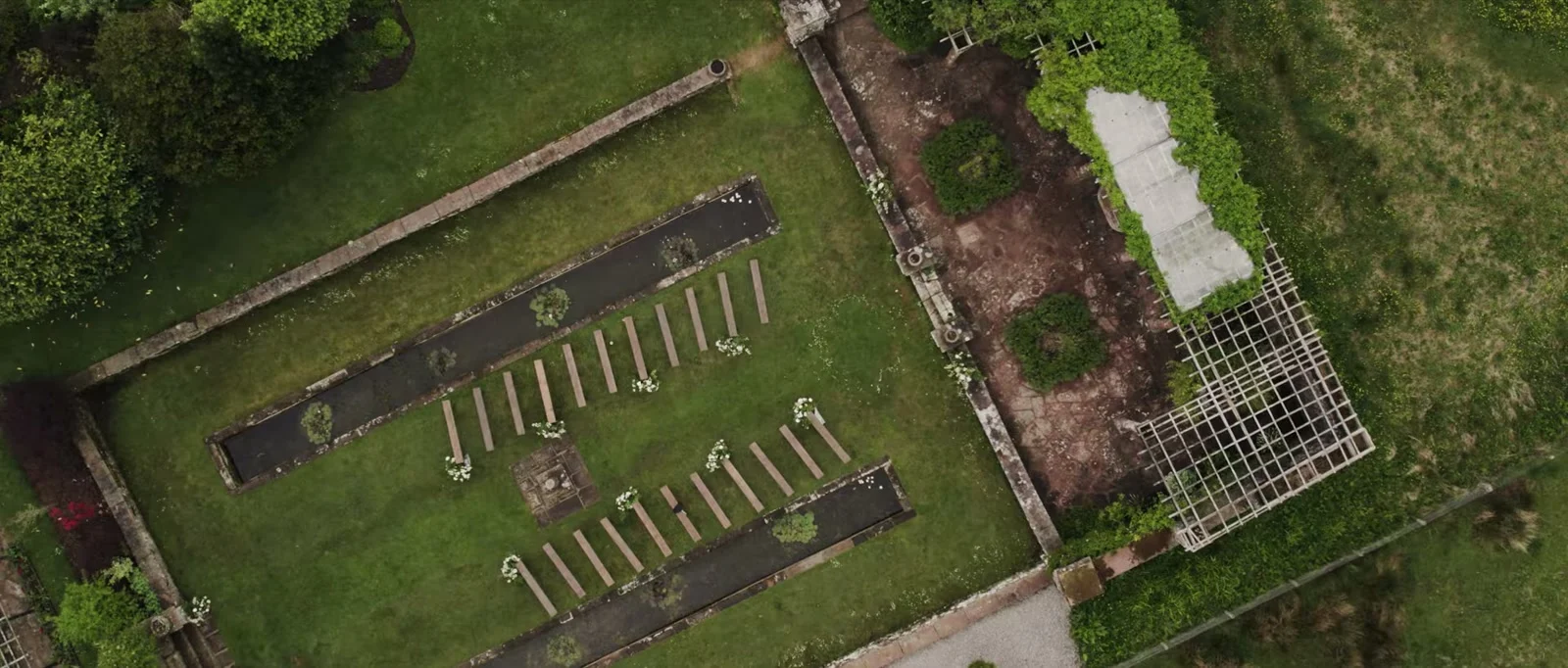 An aerial view of a walled garden with wooden benches set in two curving rows between long narrow planted beds inside old stone walls at Holesfoot