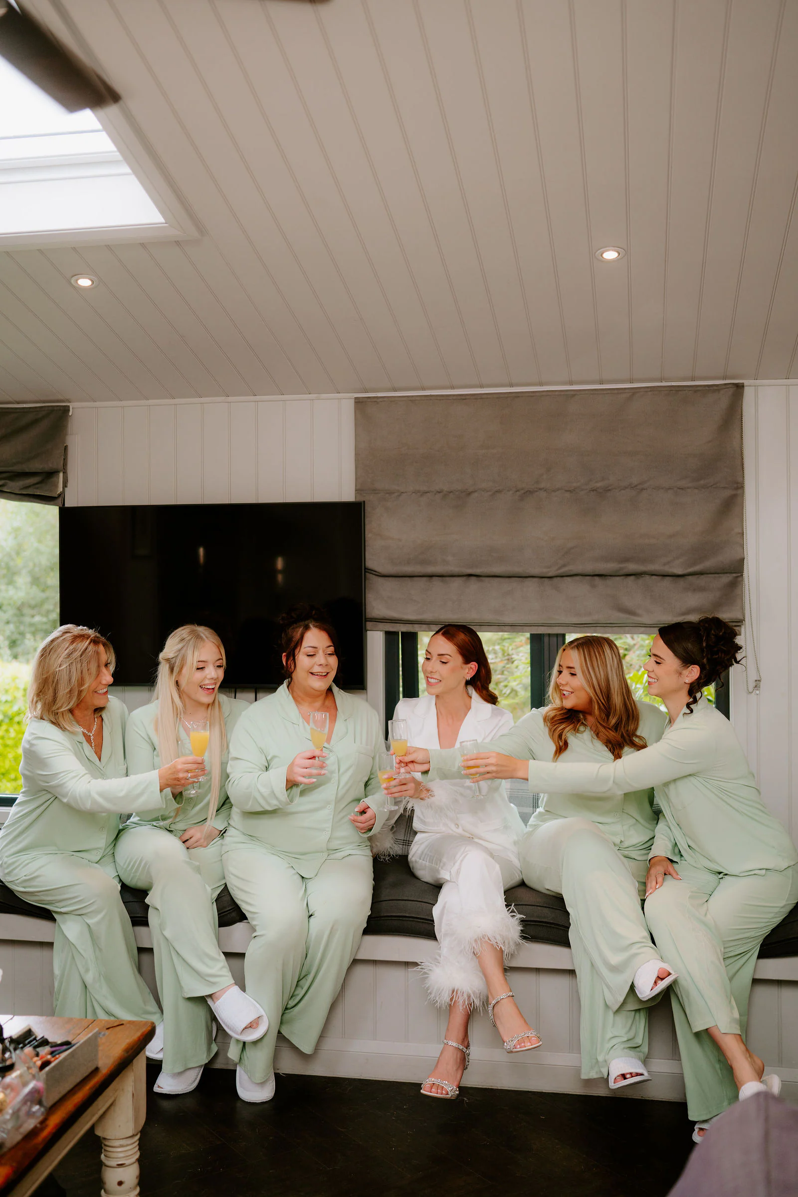 Bridesmaids in mint green pyjamas sit together on a window seat during the morning at Broadoaks near Windermere