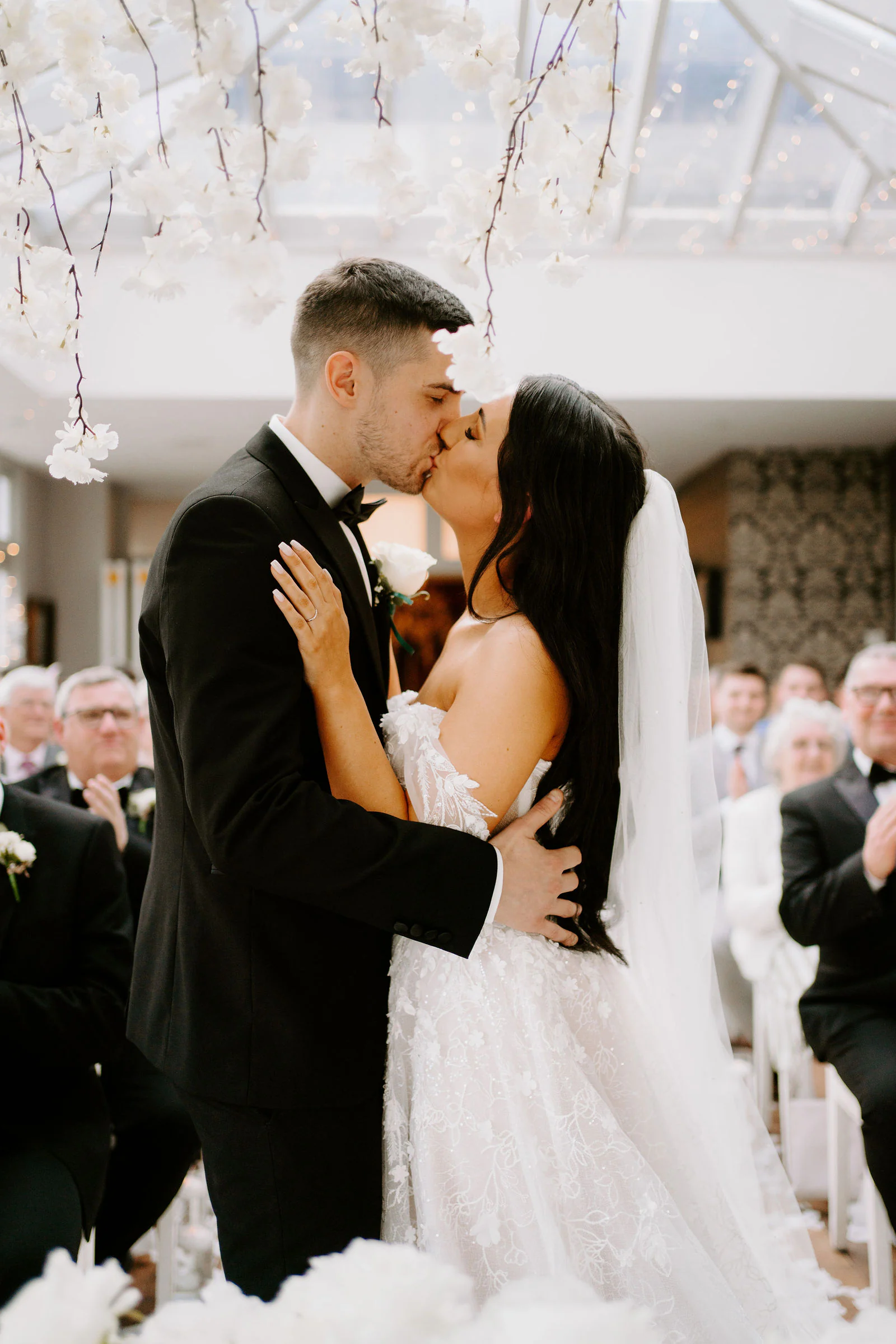 A bride and groom kiss beneath a ceiling of white flowers in the conservatory at Broadoaks Country House